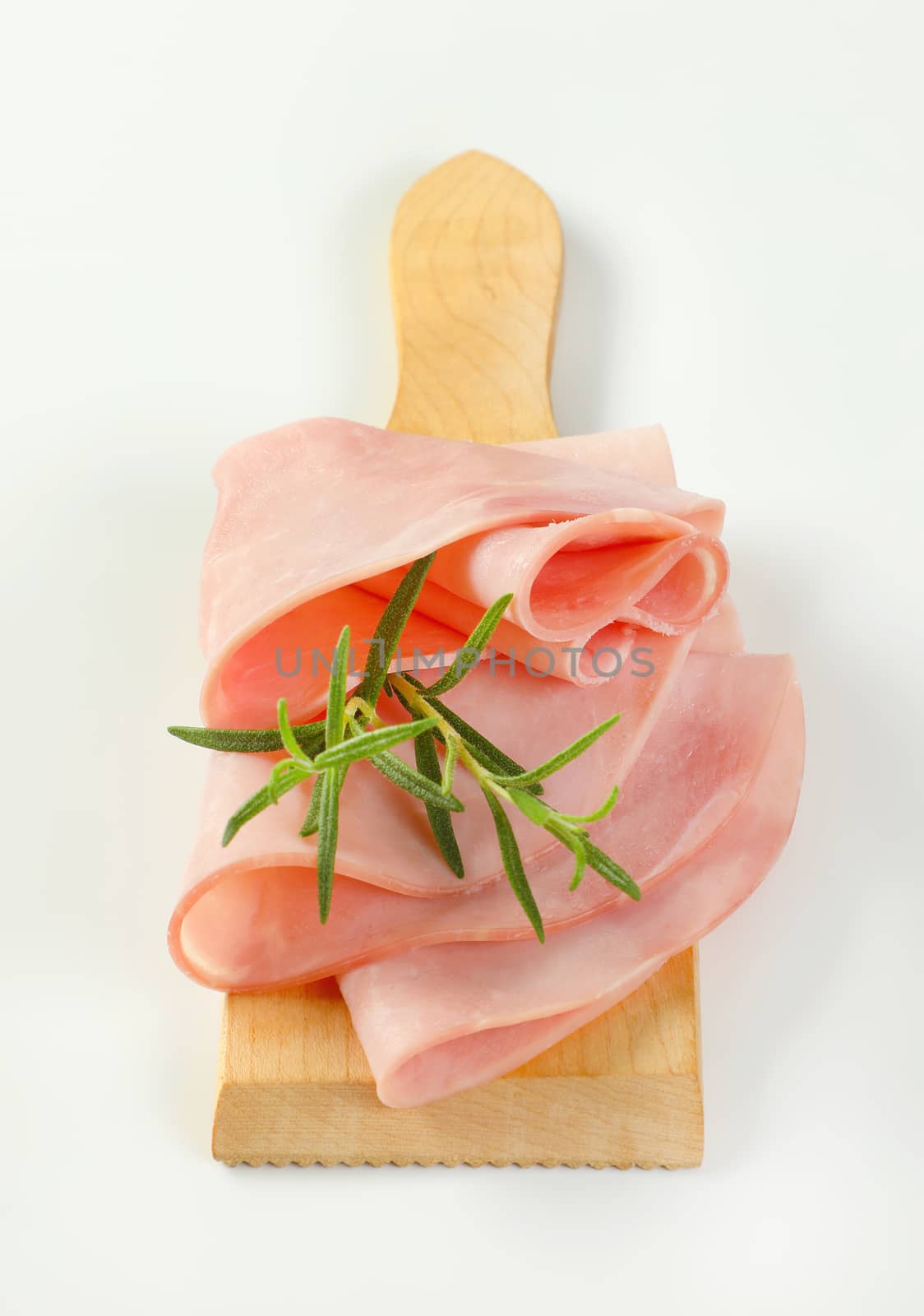 thin slices of ham and twig of fresh rosemary on wooden cutting board