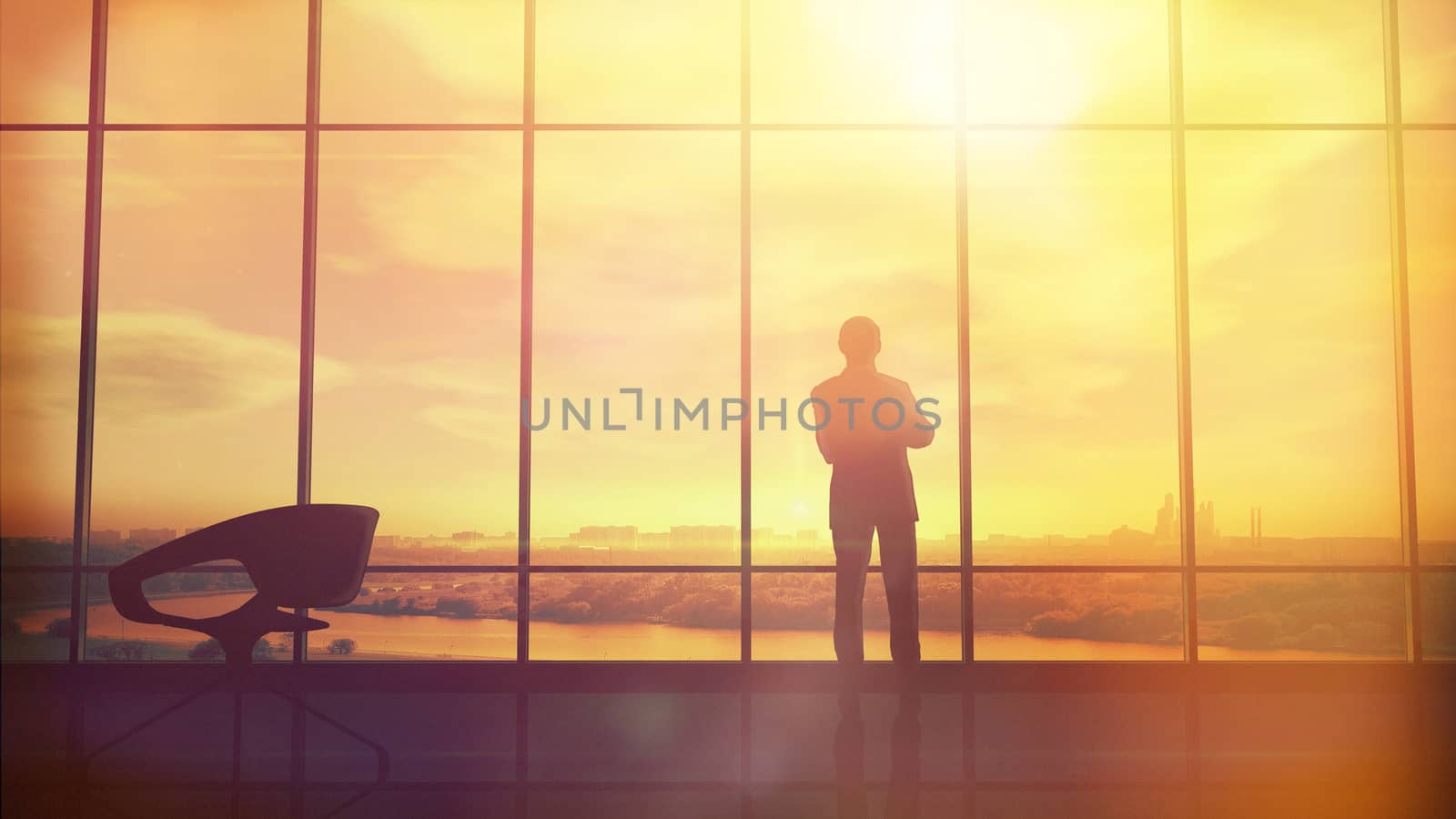 Silhouette of a man in a huge office in front of large windows.