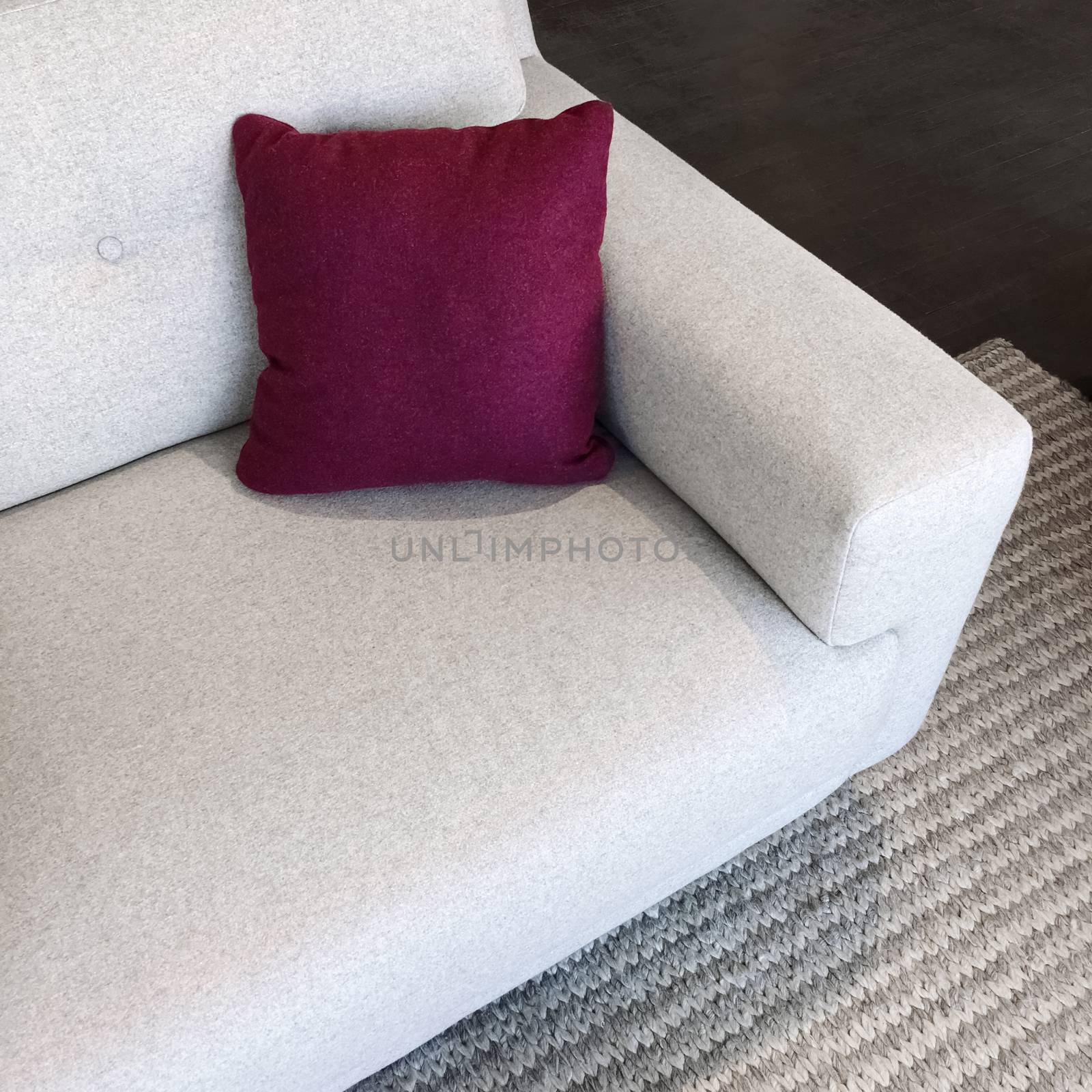 White sofa with cherry red cushion, on a gray knitted rug.