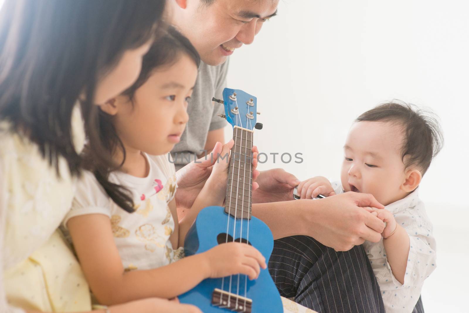 Parents and children playing ukulele together. Asian family spending quality time at home, natural living lifestyle indoors.