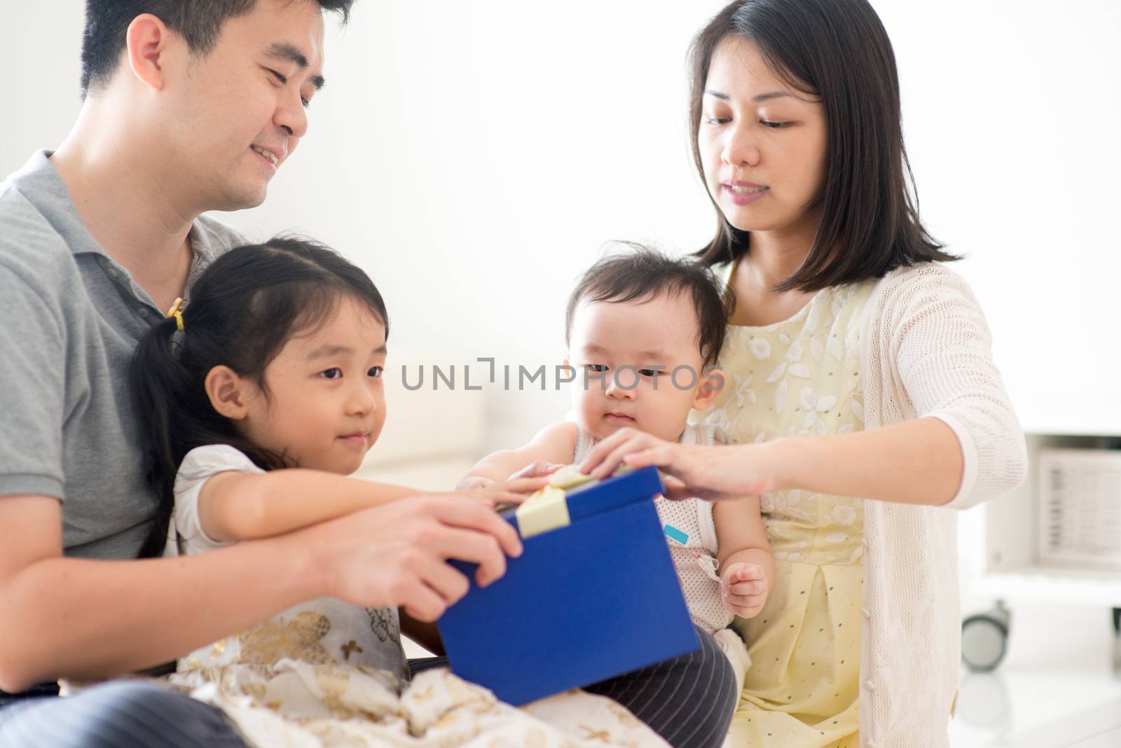Parents and children open gift box together. Asian family spending quality time at home, natural living lifestyle indoors.