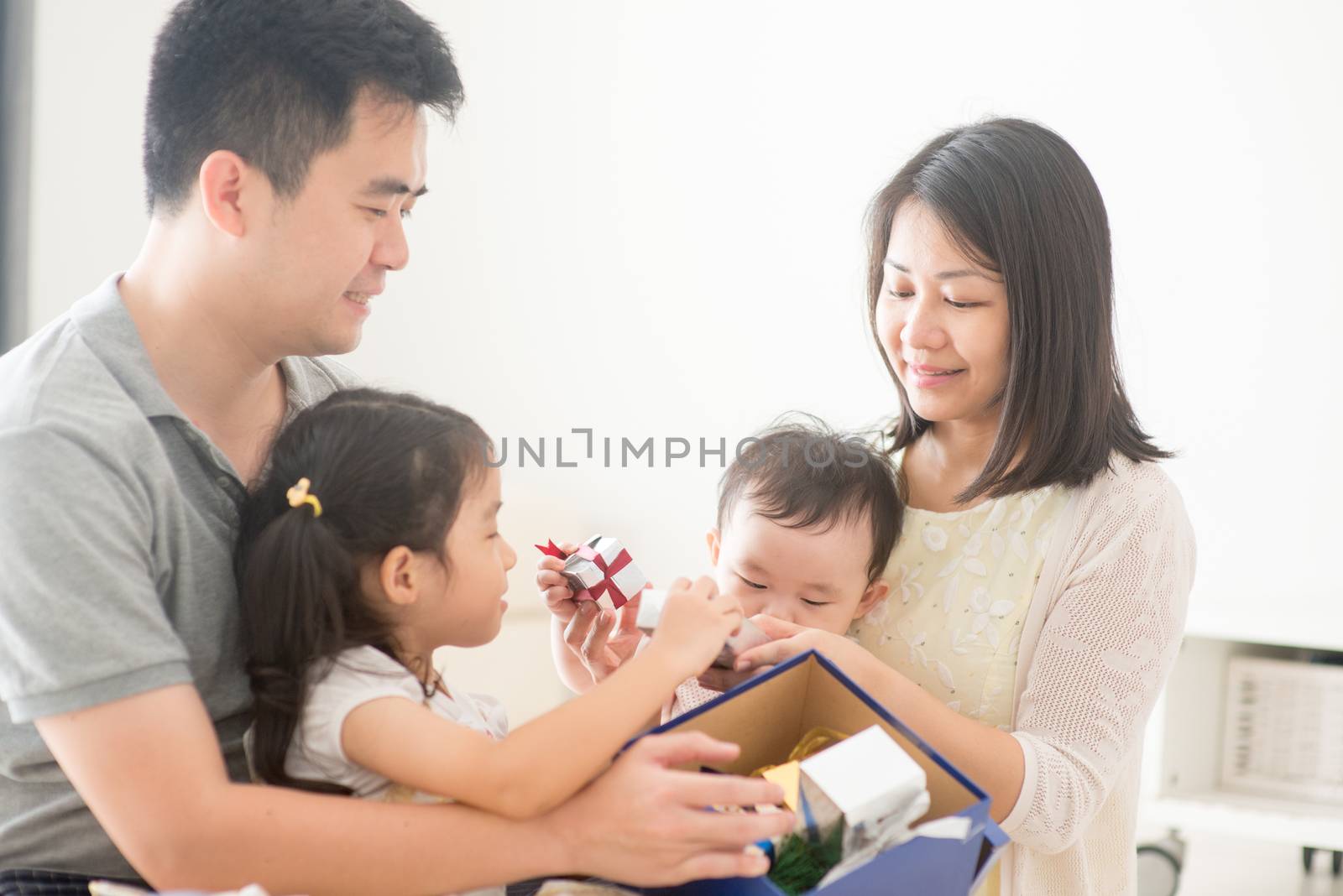 Parents and children open Christmas gift together. Asian family spending quality time at home, natural living lifestyle indoors.