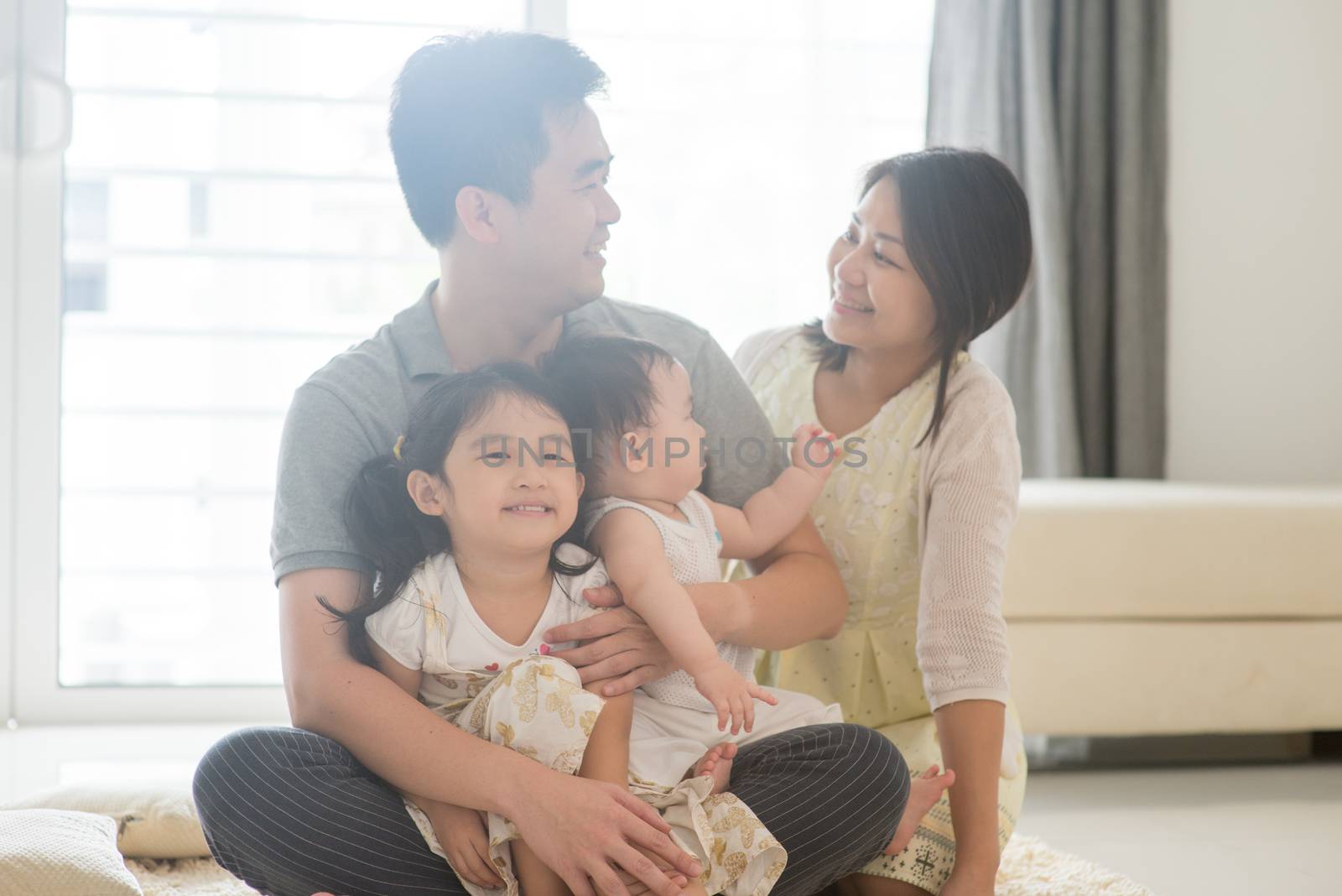 Parents and children sitting on floor together. Happy Asian family spending quality time at home, candid living lifestyle indoors.