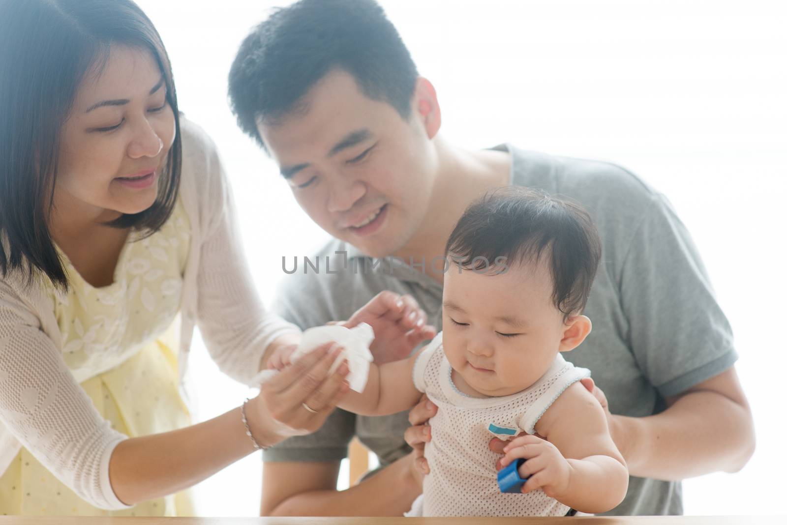 Mother wipes baby hand with tissue paper. Asian family spending quality time at home, living lifestyle indoors.