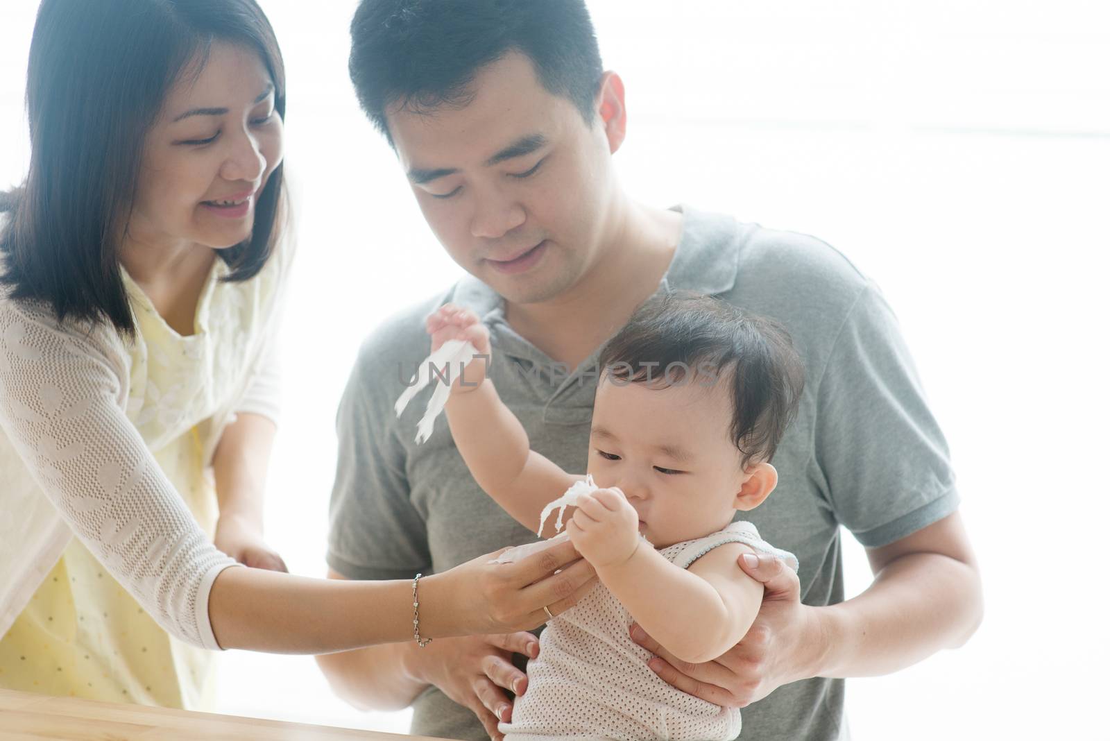 Mother wipes baby hand with tissue paper. Asian family spending quality time at home, living lifestyle indoors.