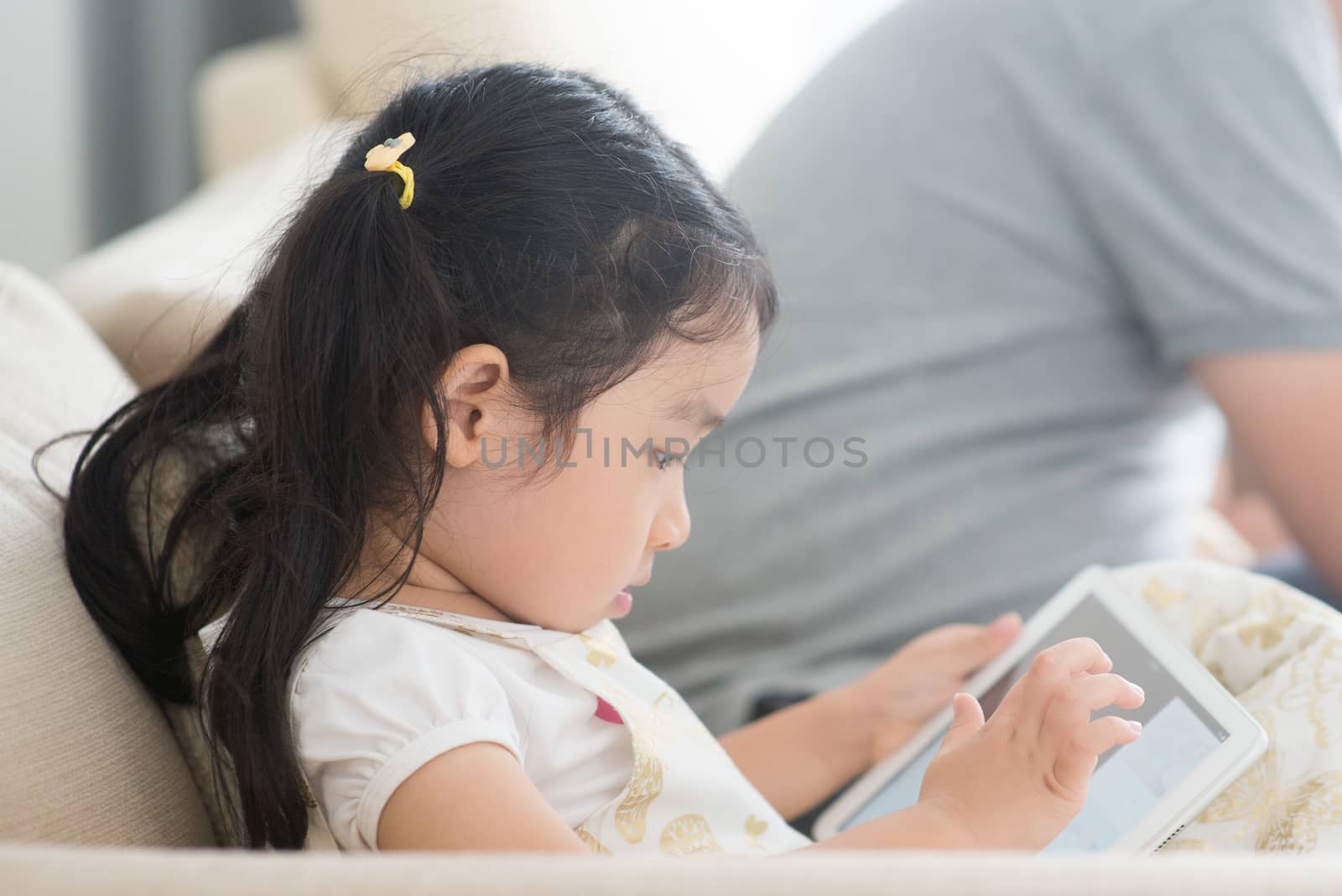 Little girl using digital tablet on sofa. Asian family at home, living lifestyle indoors.