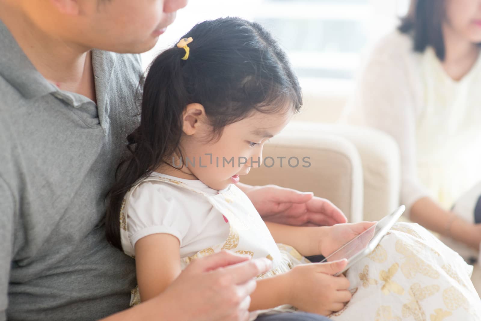  Father and child playing with digital tablet on sofa. Asian family at home, living lifestyle indoors.