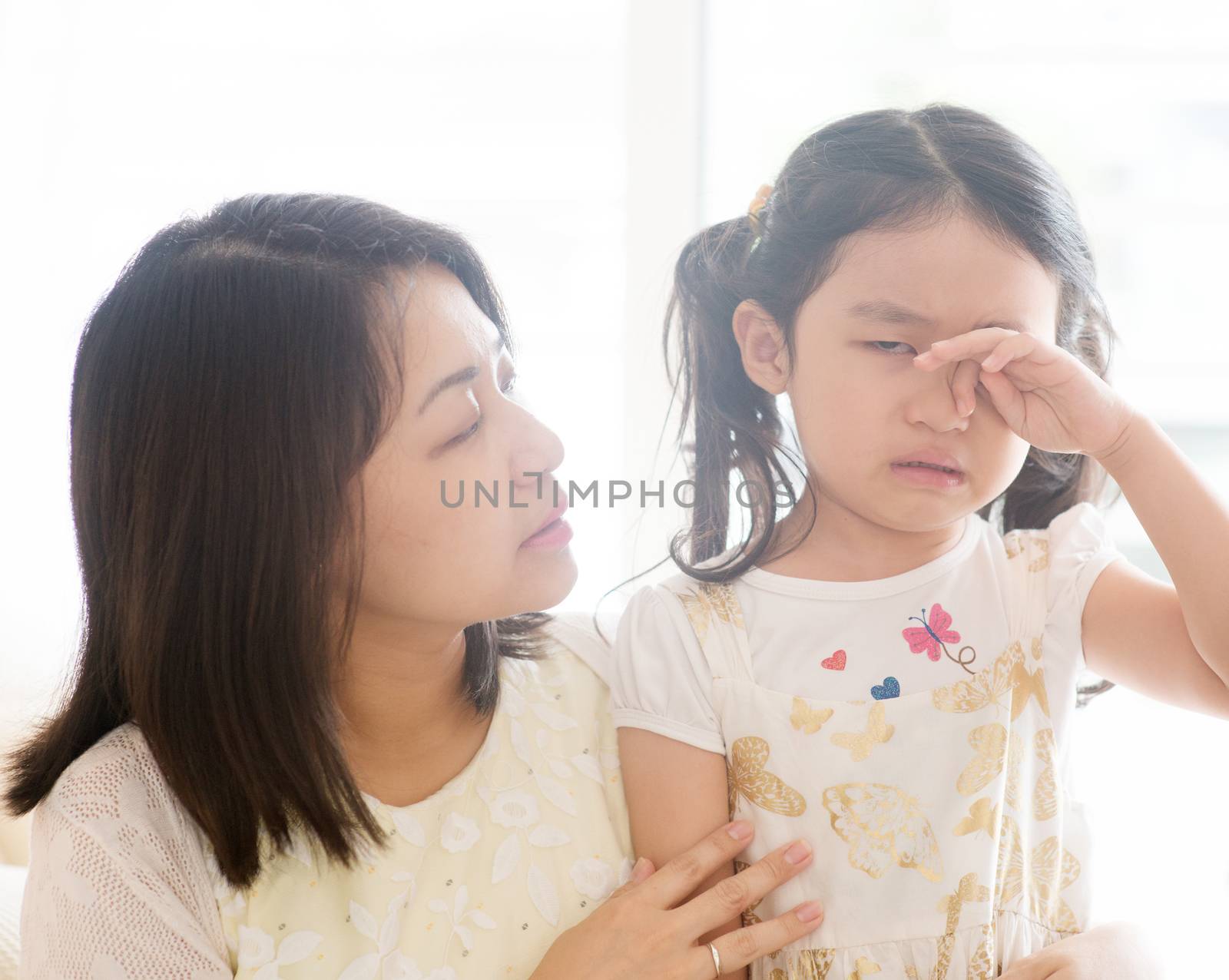 Mother comforting crying daughter. Asian family at home, living lifestyle indoors.