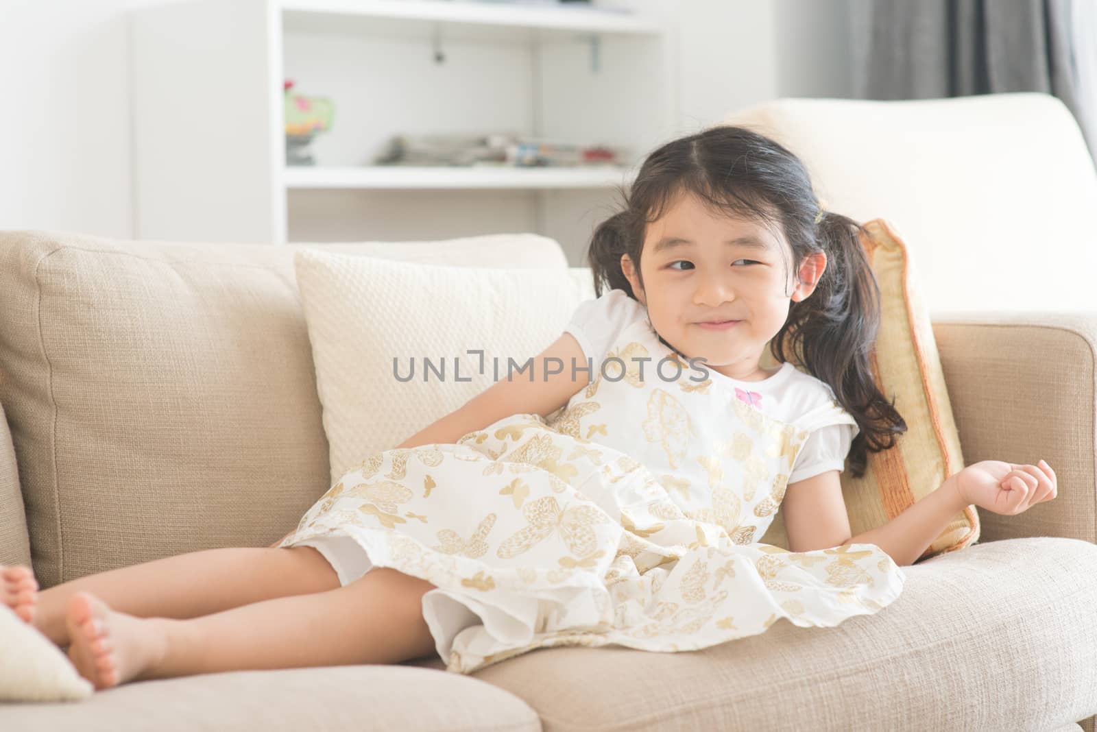 Little girl lying on sofa and watching tv. Asian family at home, living lifestyle indoors.