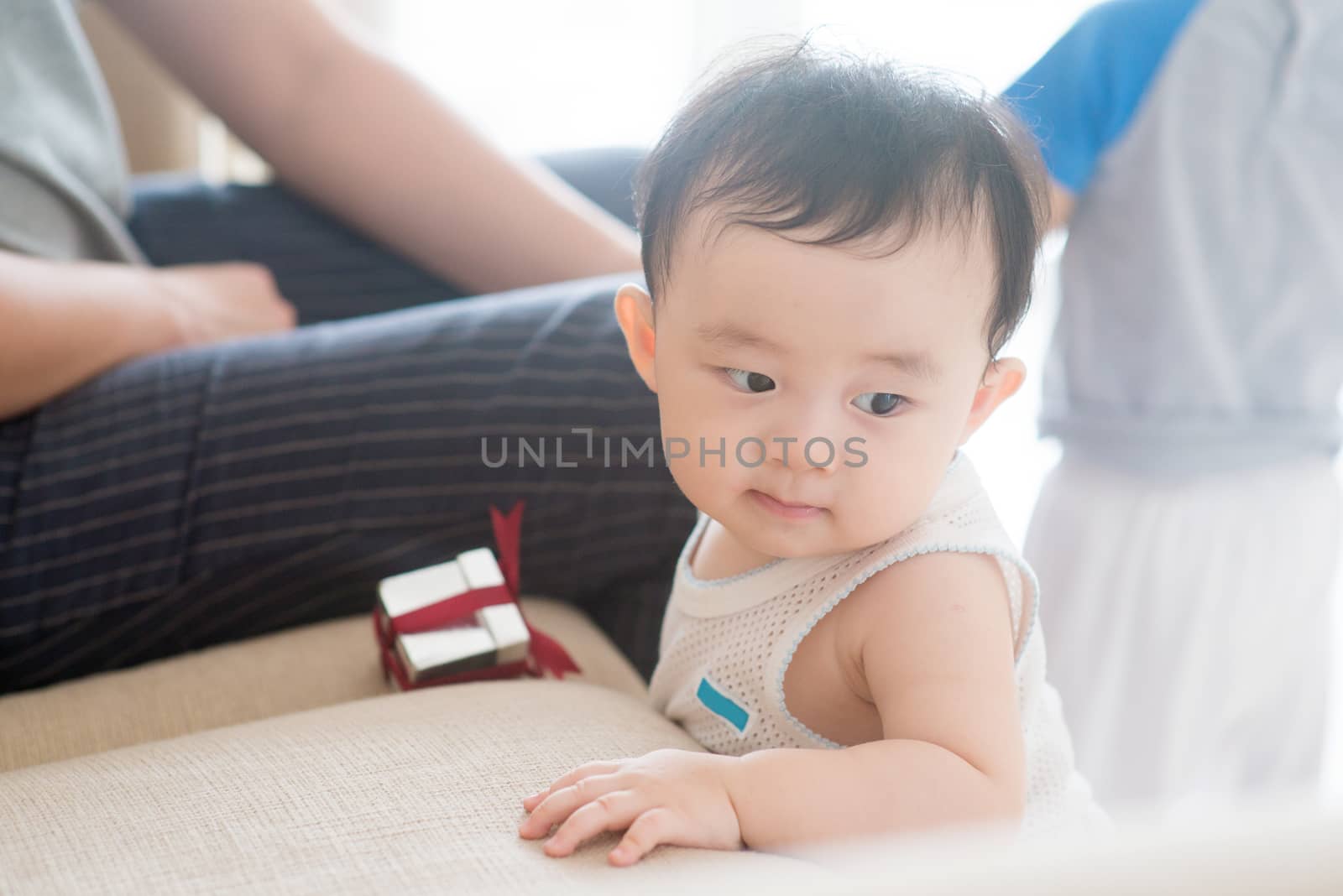 Nine months old baby boy holding sofa and learning how to walk. Asian family at home, living lifestyle indoors.