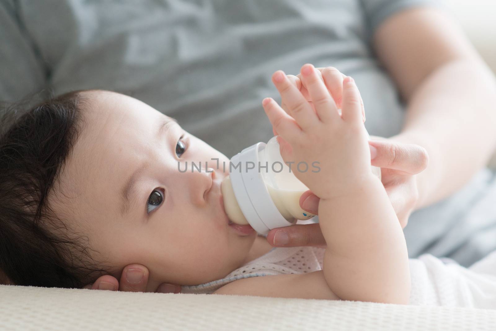 Happy Asian family at home. Father bottle feed formula milk to 9 months old toddler, living lifestyle indoors. 