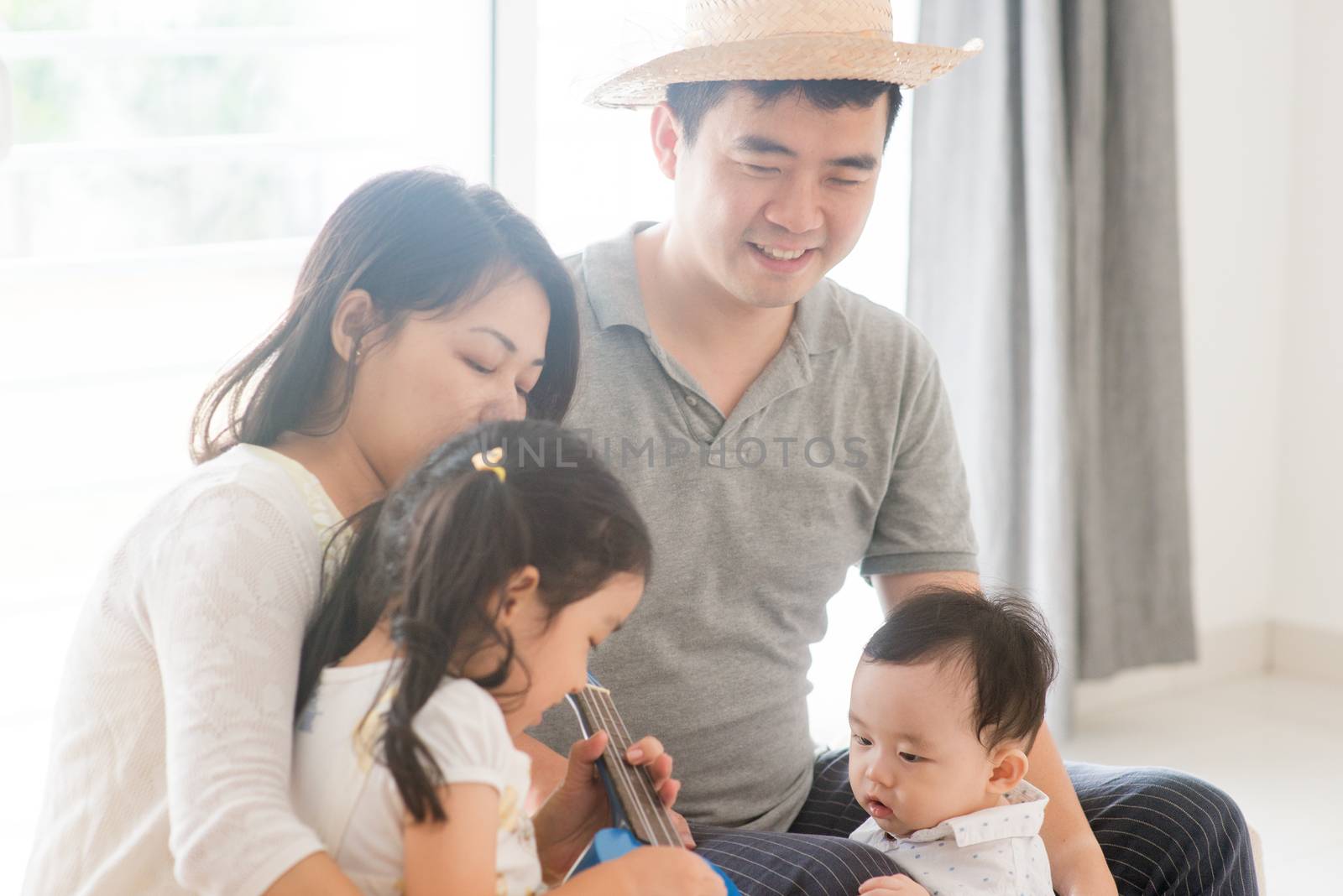 Parents and children singing and playing ukulele together. Asian family spending quality time at home, living lifestyle indoors.