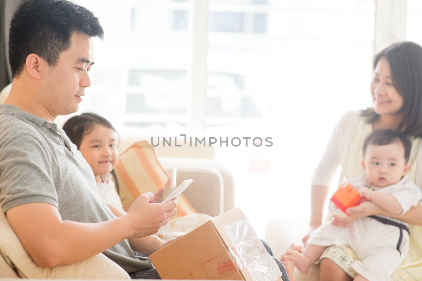 Chinese man scanning QR code with smart phone. Happy Asian family at home, natural living lifestyle indoors.