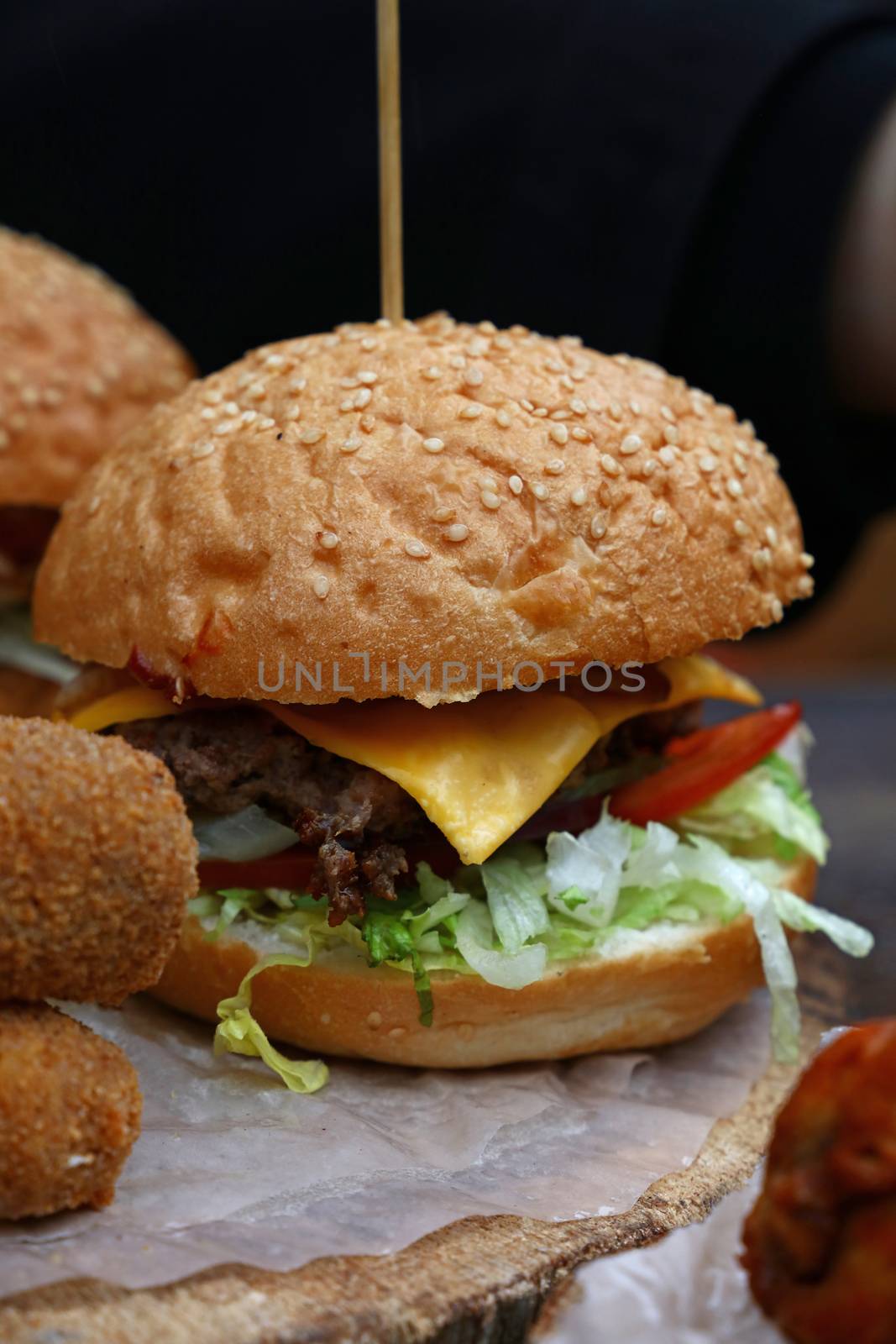 Big American cheese burger with pulled pork meat and salad in sesame bun on paper parchment over natural wooden cut, close up, low angle view