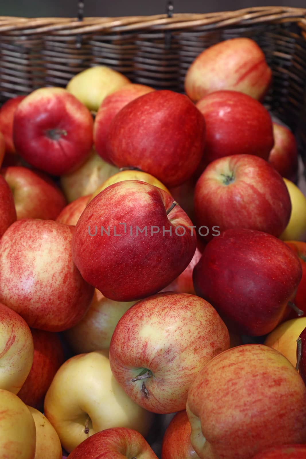 Heap of fresh red and yellow ripe apples in wicker wooden basket on retail market stall display, close up, high angle view
