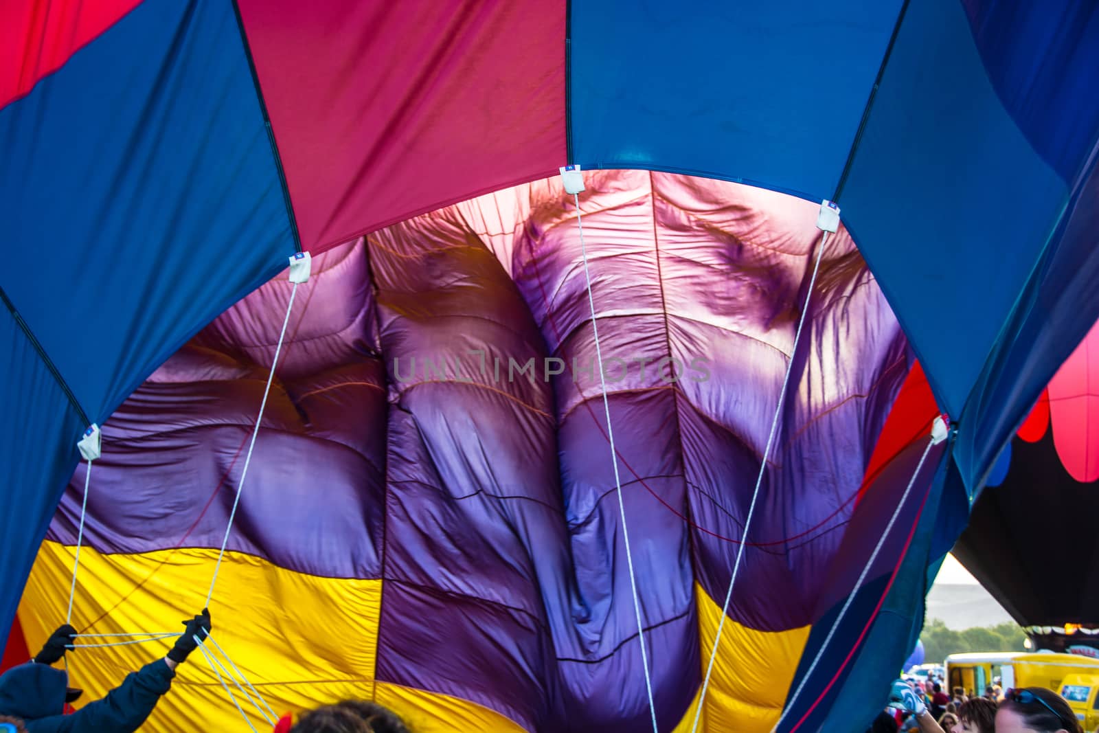 Ground crew holds guys whil the burner inflates this colorful hot air balloon