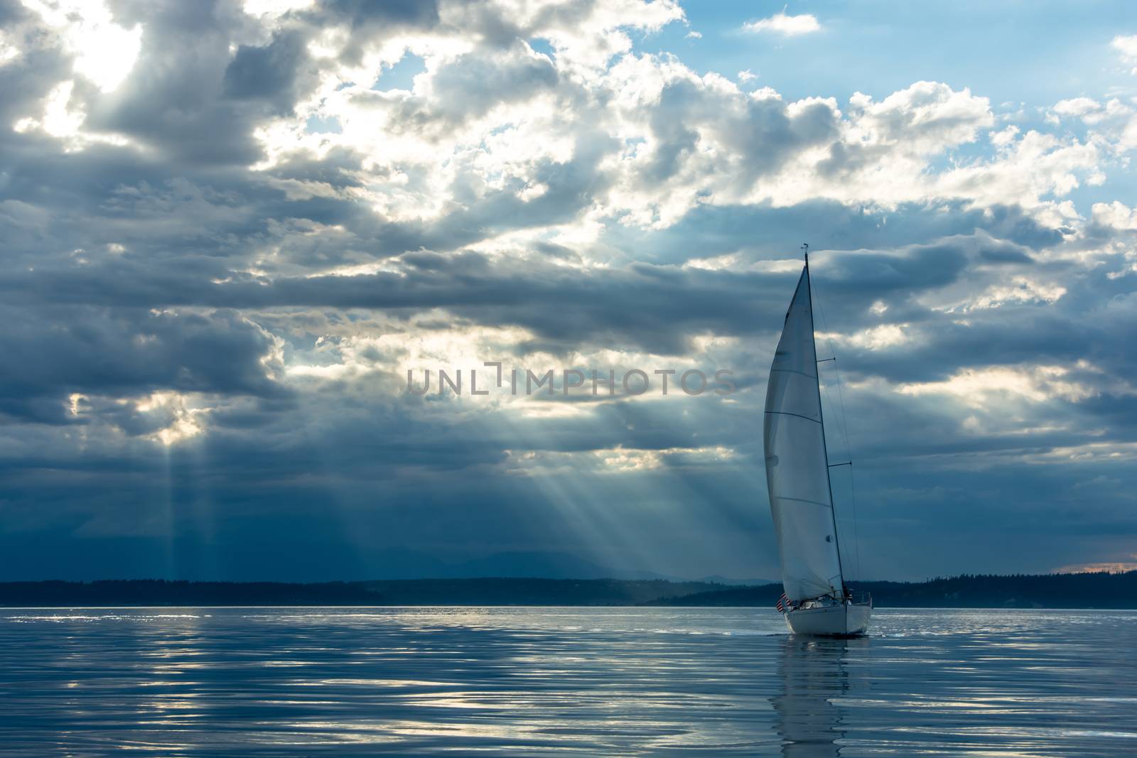 Magic rays penetrate clouds at sunset behind sailboat.