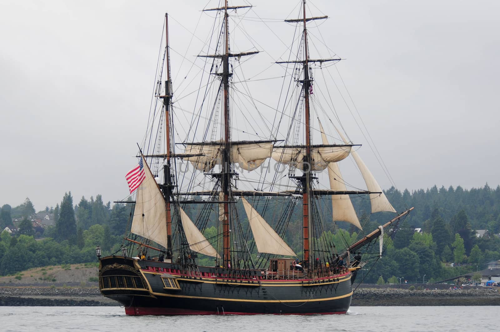 Replica of HMS Bounty with minimal sail under overcast sky.