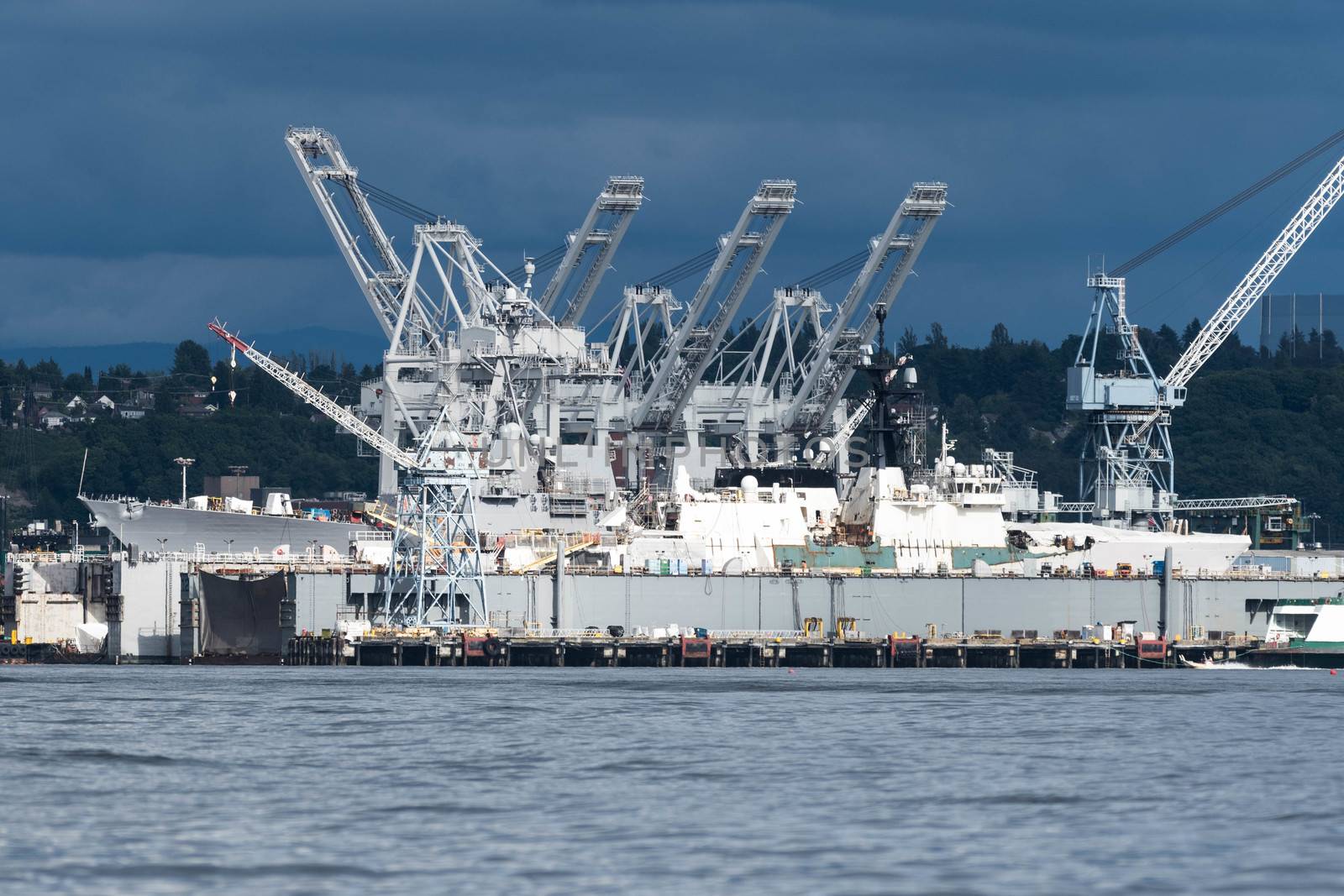 US Navy ship and US Coast Guard ships being worked on at Seattle's  largest shipayard on cloudy day with bright sunlight.