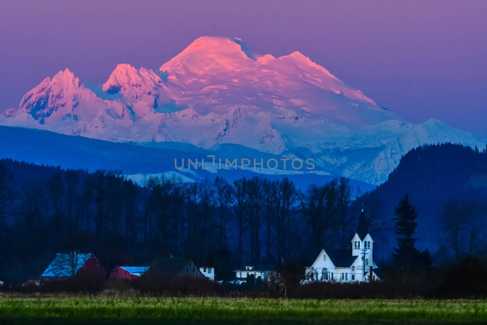 Snow capped Mount Baker at twilight across open field with church in the middle ground