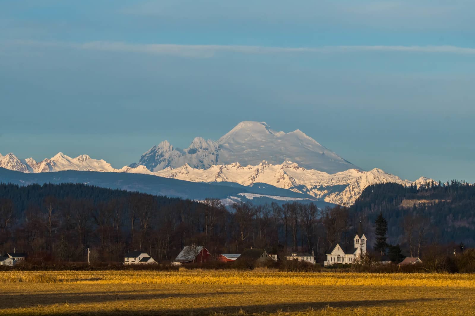 Snow capped Mount Baker across open field with church in the middle ground