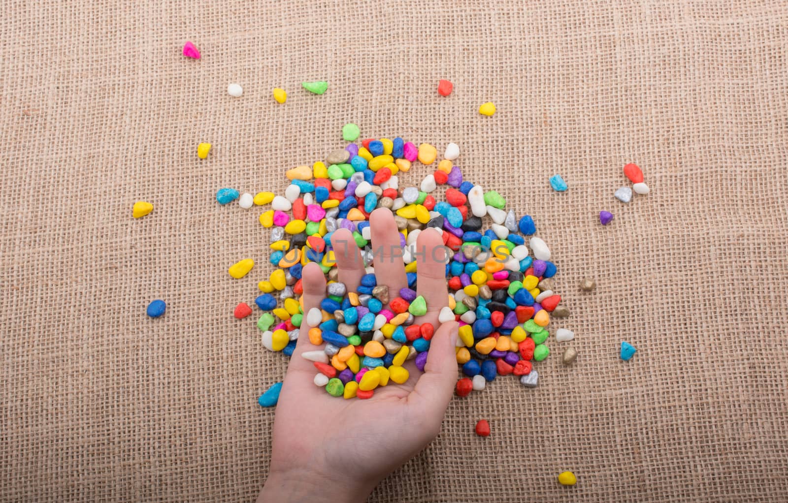 Colorful little pebbles in hand and on canvas ground