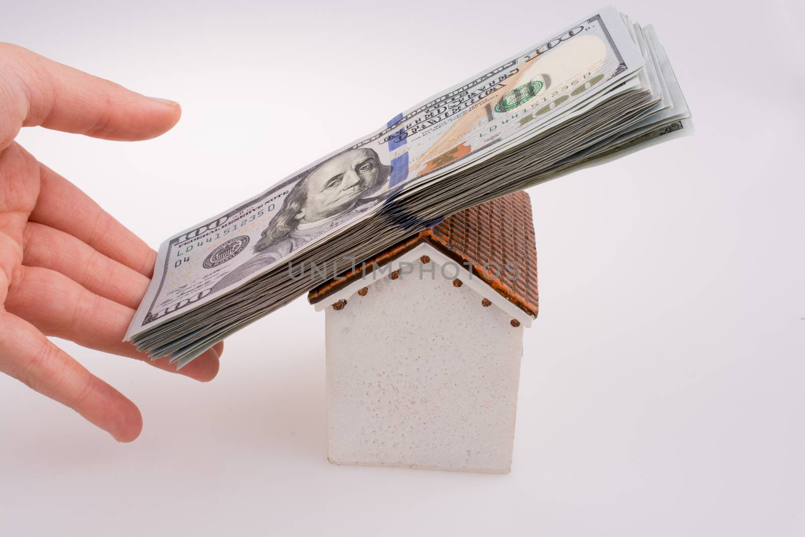 Hand holding American dollar banknotes on the roof of a model house  on white background