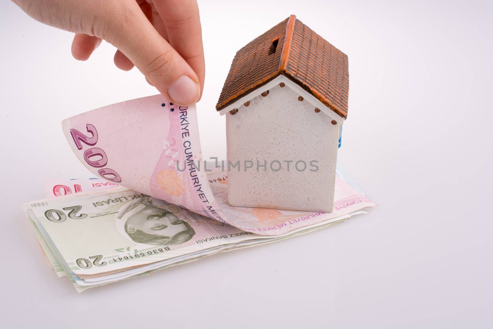 Hand holding Turkish Lira banknotes by the side of a model house by berkay