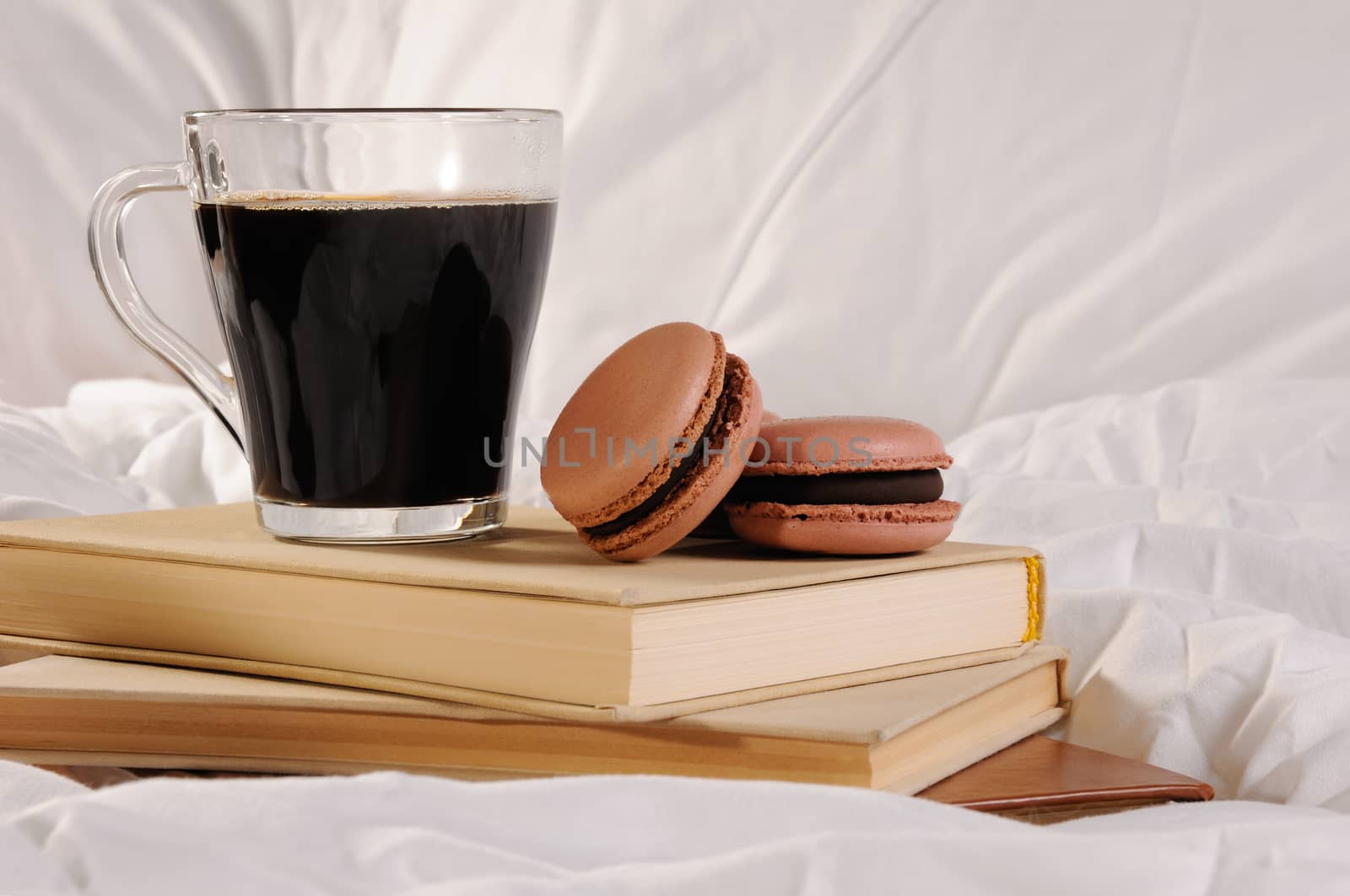 Morning cup of coffee with chocolate cakes Macaroons, on a pile of books in bed.