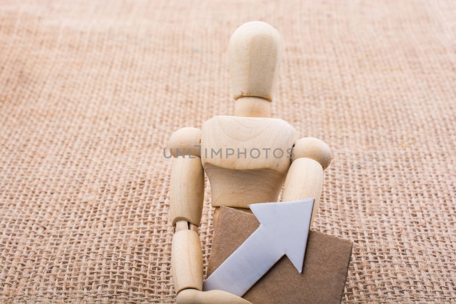 Wooden man holding a paper arrow on canvas