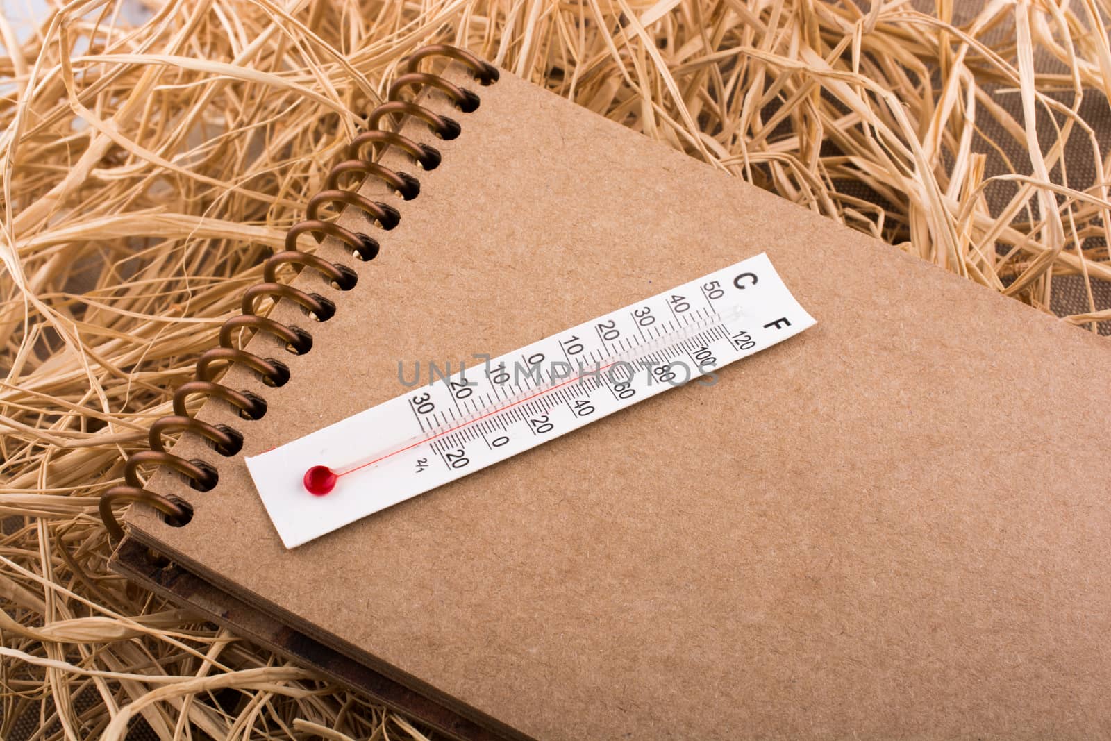 Thermometer on a brown notebook on a straw background