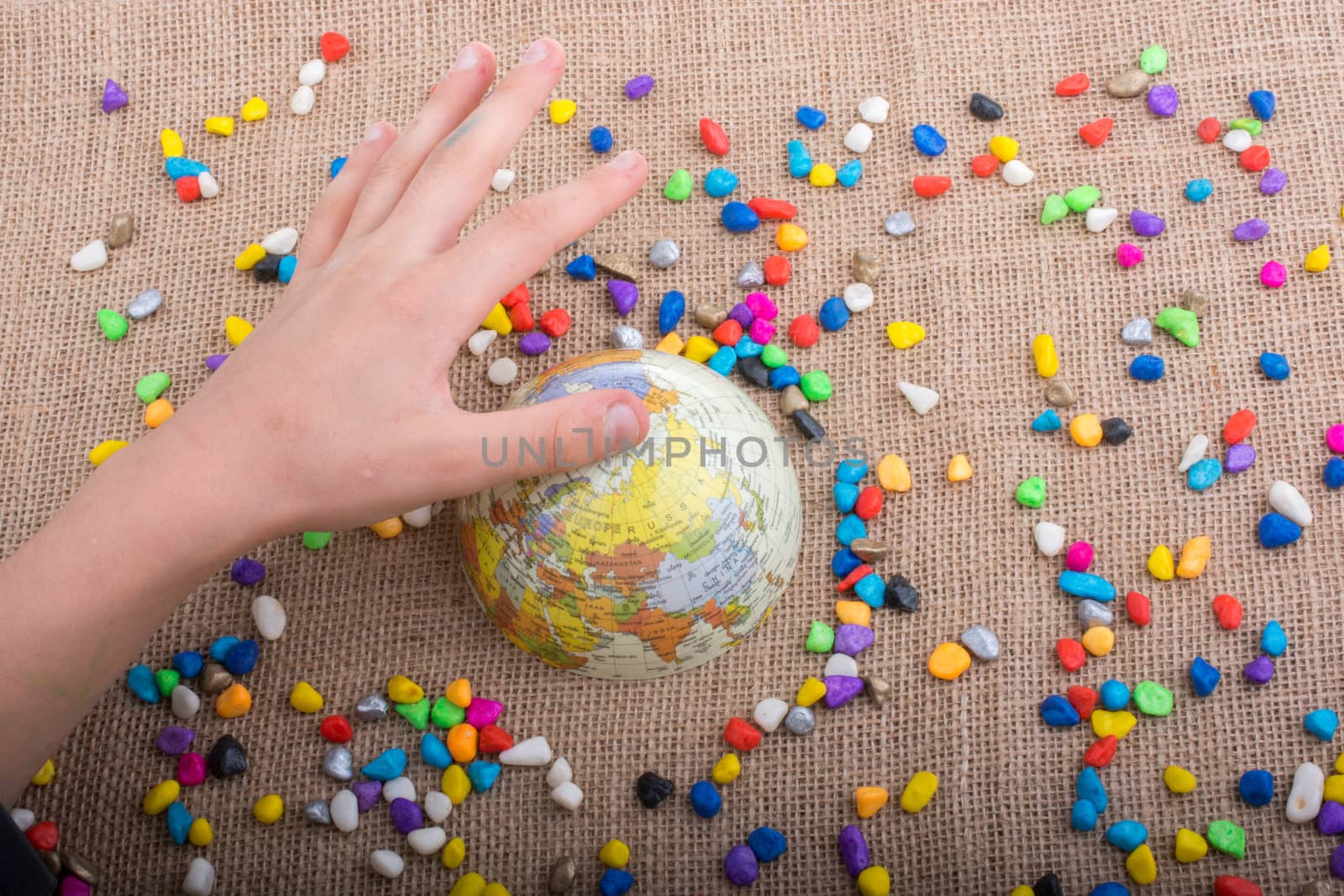 Hand holding globe placed amid colorful pebbles