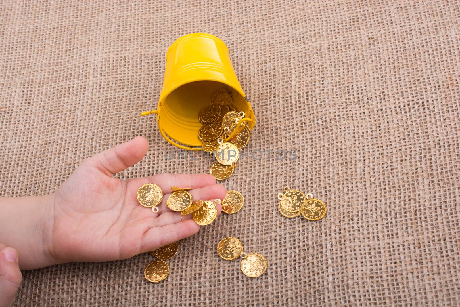 Bucket and fake gold coins in hand on canvas background