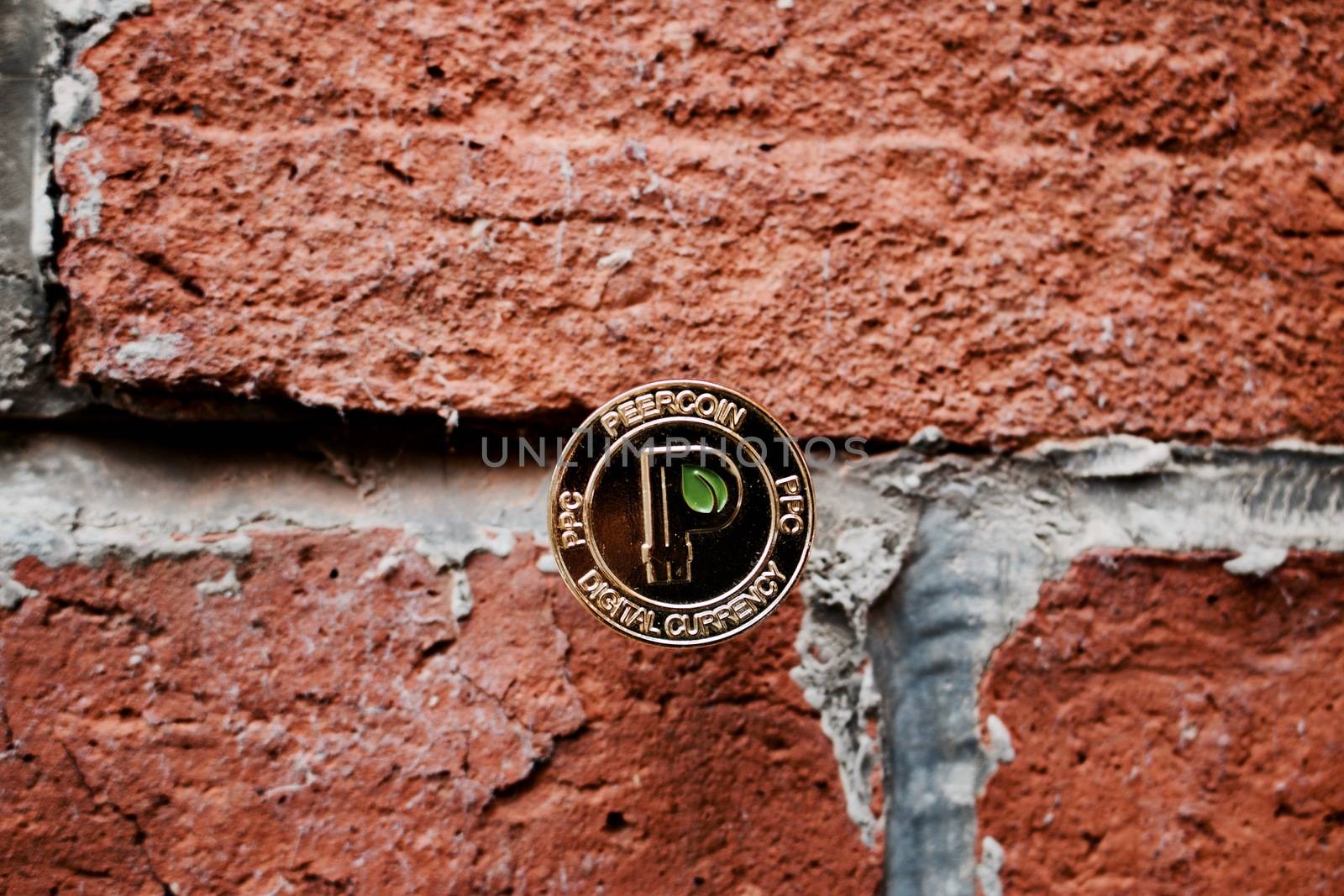 Digital currency physical gold peercoin with green leaf on the brick wall.