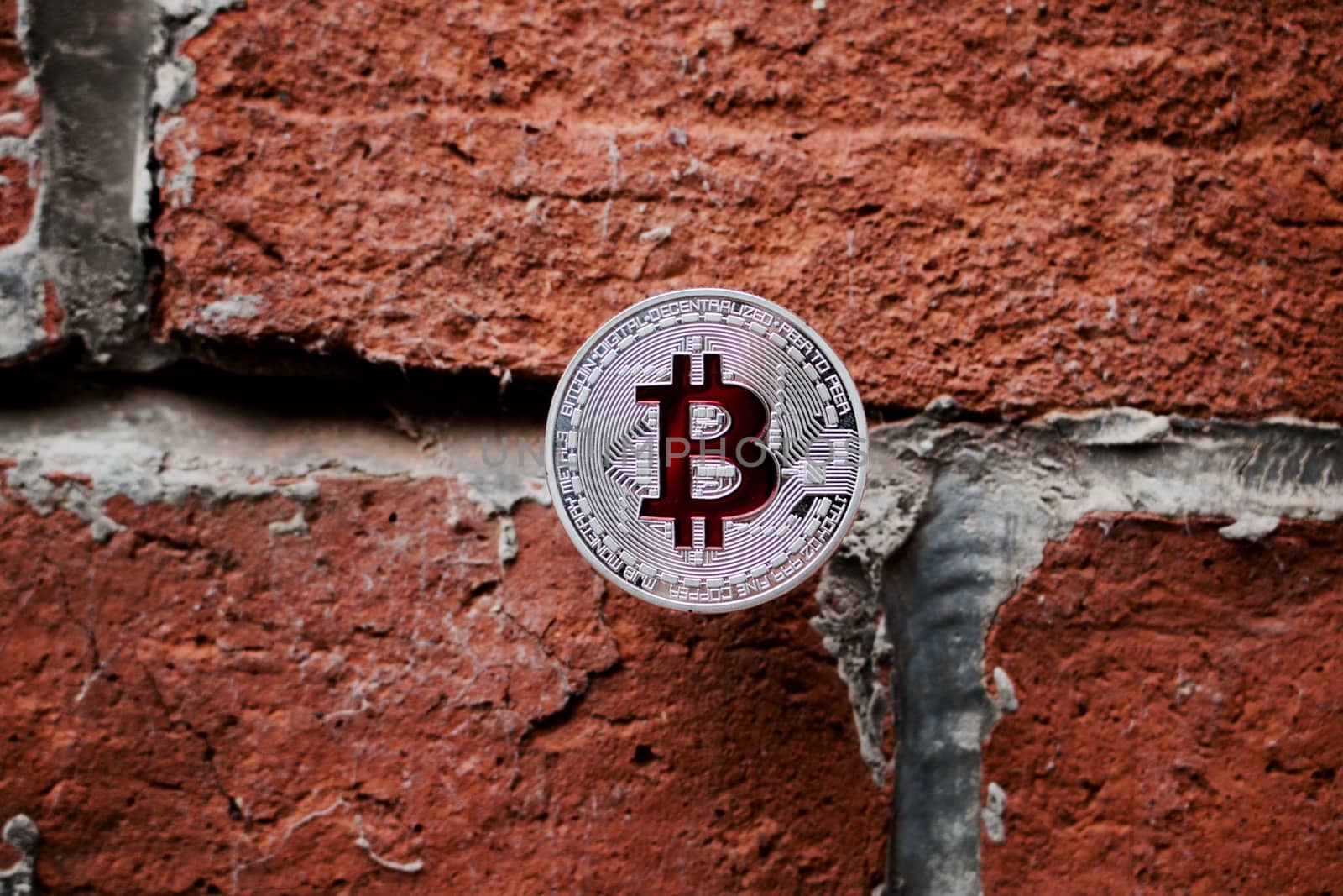 Cryptocurrency physical silver bitcoin coin with red sign on the brick wall.