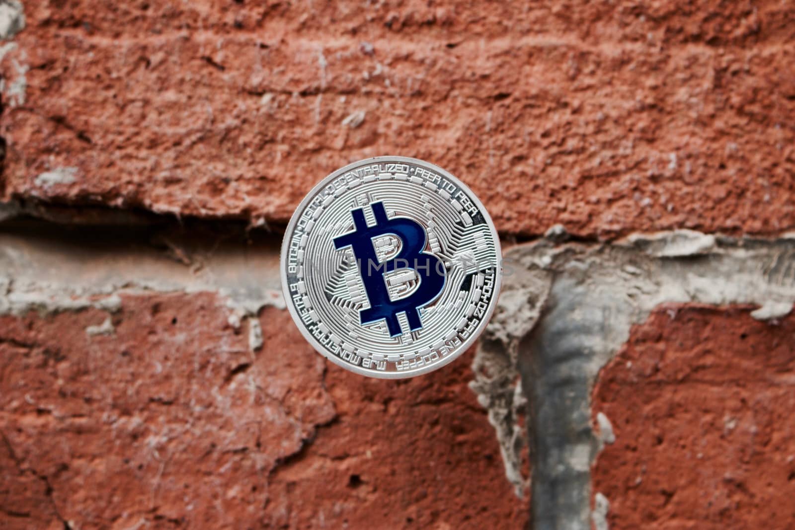 Digital currency physical silver bitcoin coin with blue sign on the brick wall.