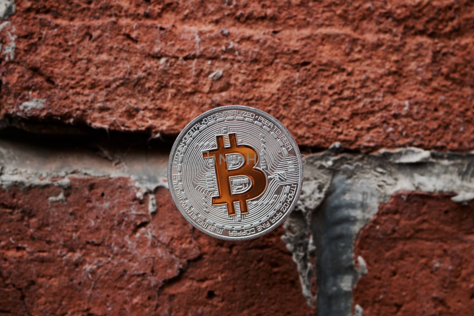 Digital currency physical silver bitcoin coin with yellow sign on the brick wall.