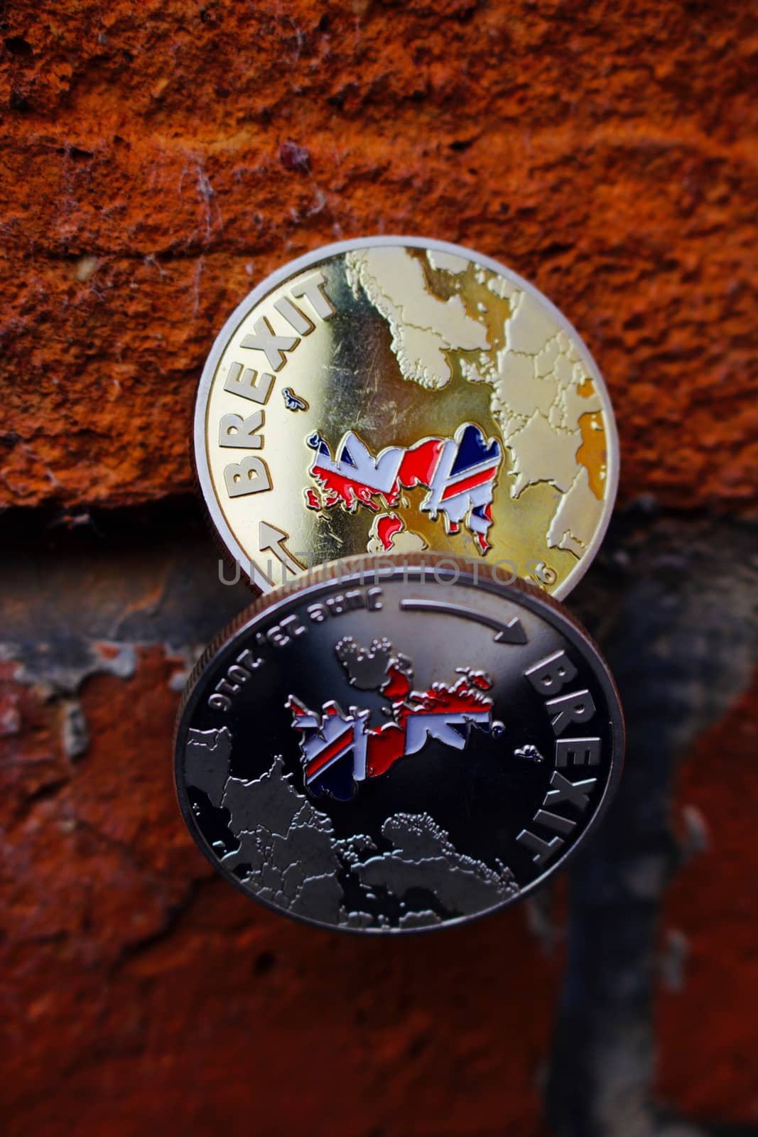 Two coins. Gold and silver brexit money with british map on brick wall.