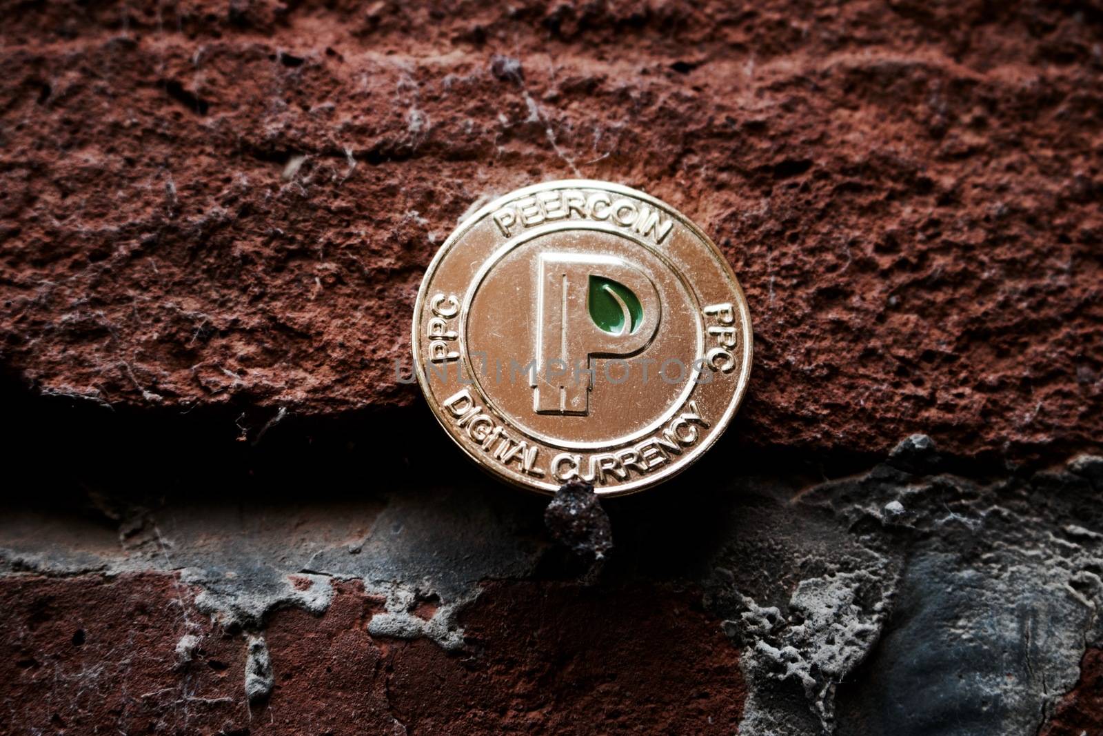 Cryptocurrency physical gold peercoin coin with green leaf in sign on black brick wall.