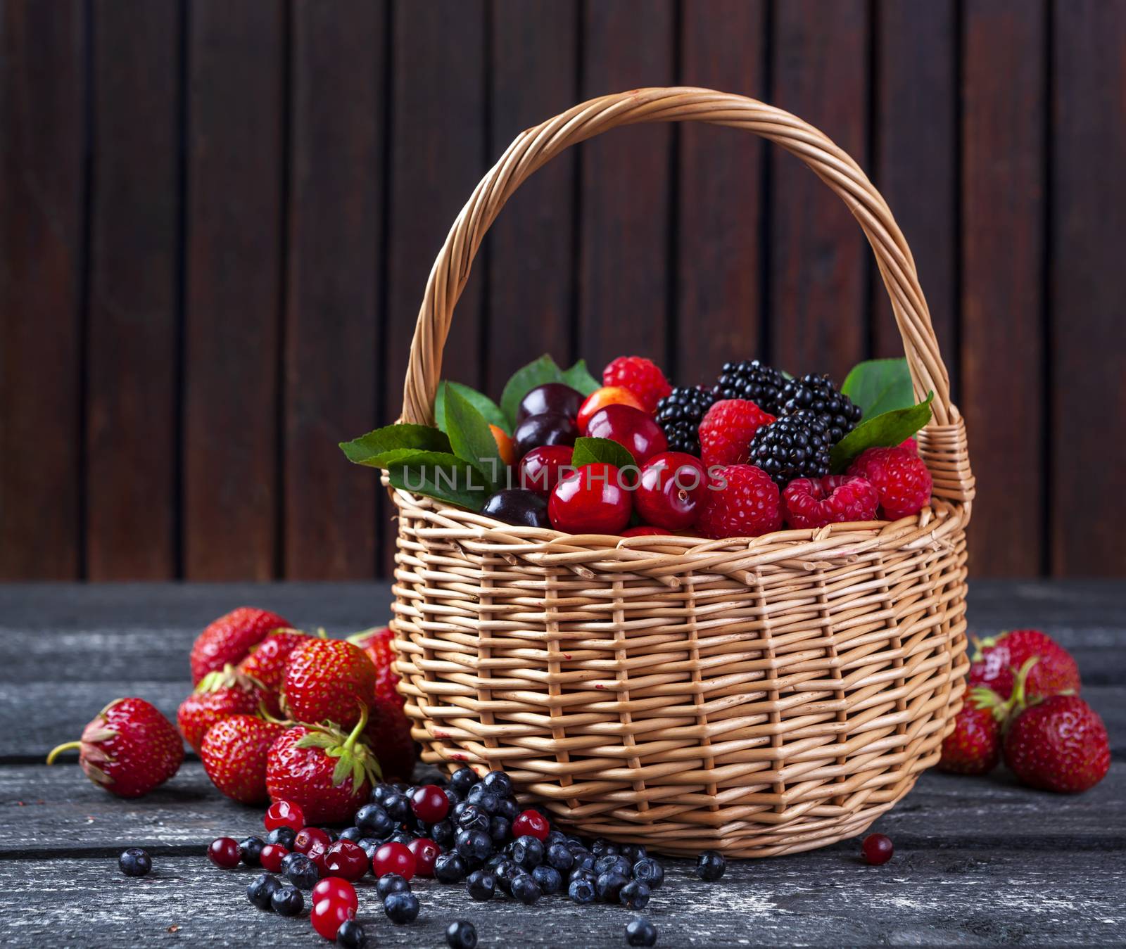 Fresh forest berries in basket on rustic wooden background. Copy space