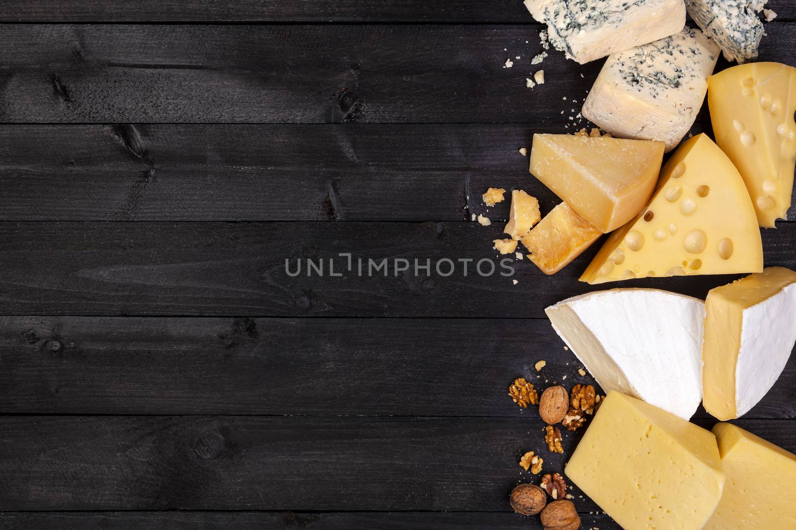 Various types of cheese on black wooden table background. Cheddar, parmesan, emmental, blu cheese. Top view, copy space.
