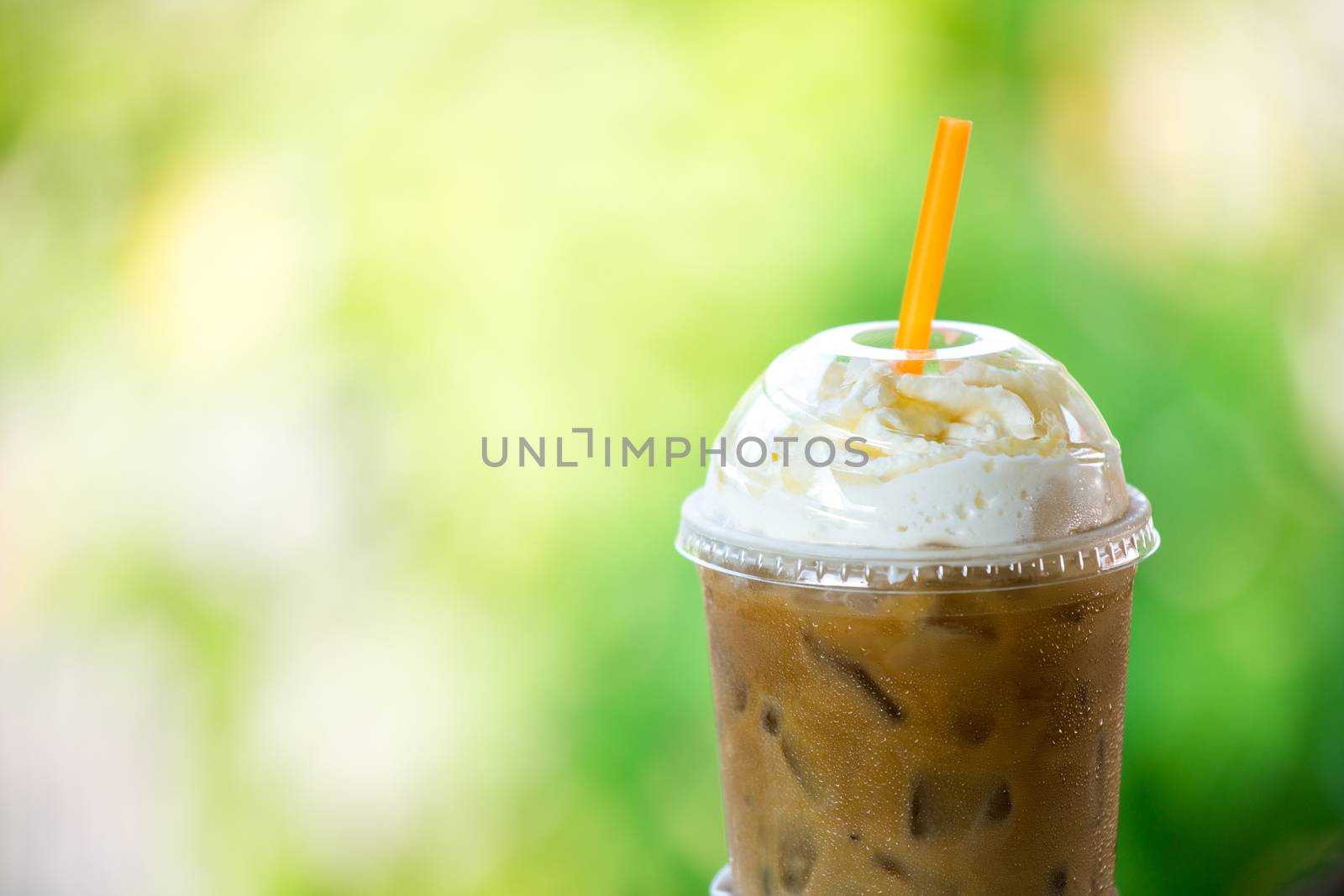 iced coffee with whipped cream in plastic cup on the garden table