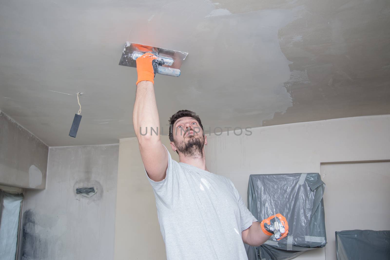 A worker with protective gloves is plastering the ceiling.