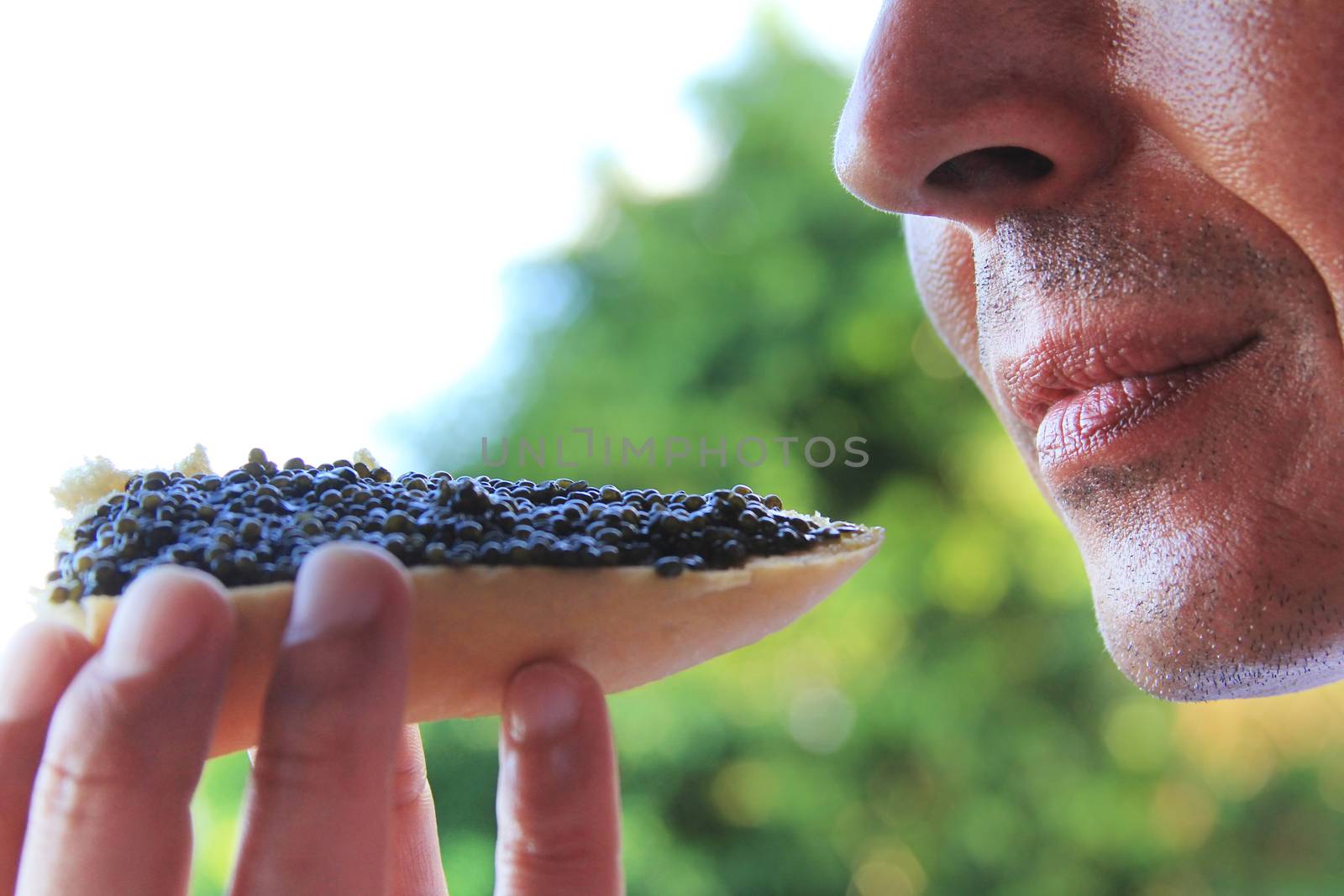 Adult man eating a sandwich with black caviar by friday