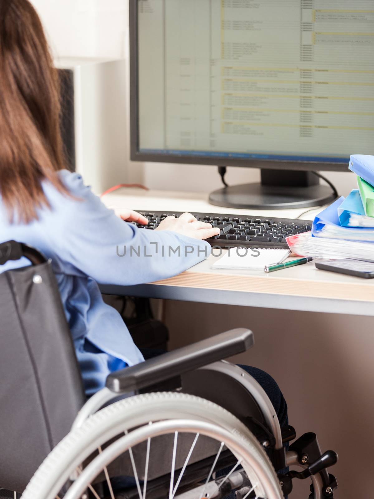Invalid or disabled woman sitting wheelchair working office desk computer by ia_64