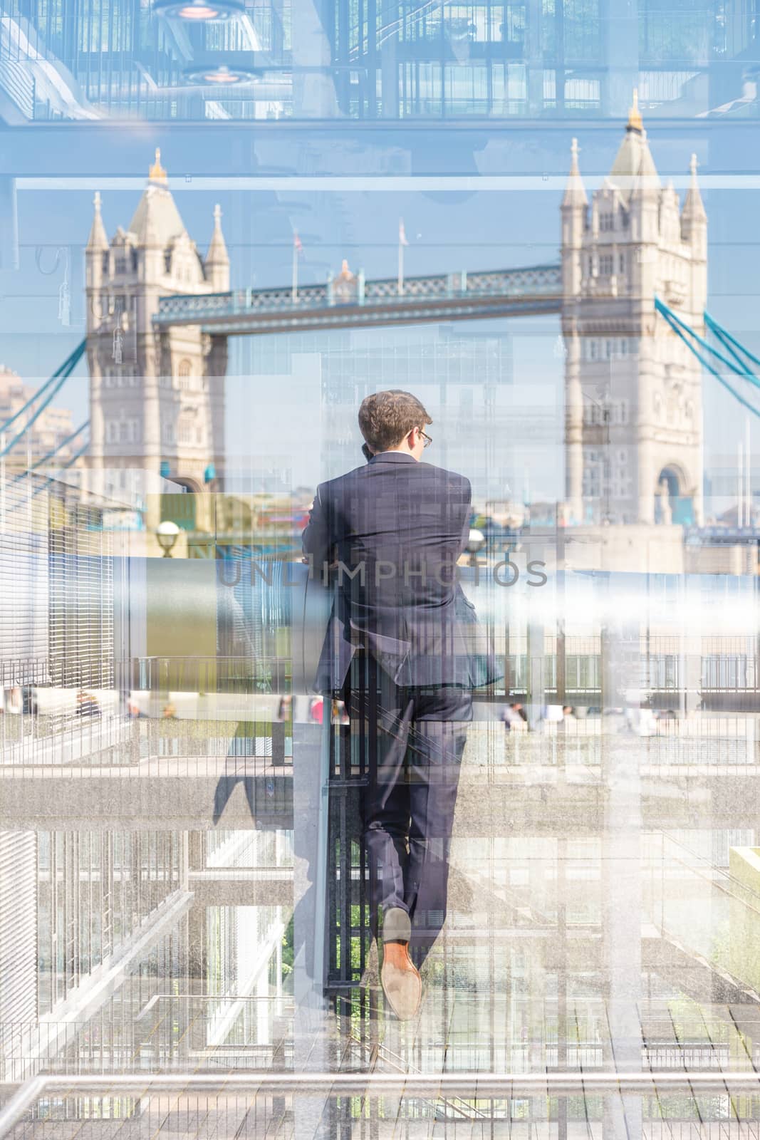 Businessman talking on mobile phone while looking trought the business office window at Tower Bridge in London city, UK.