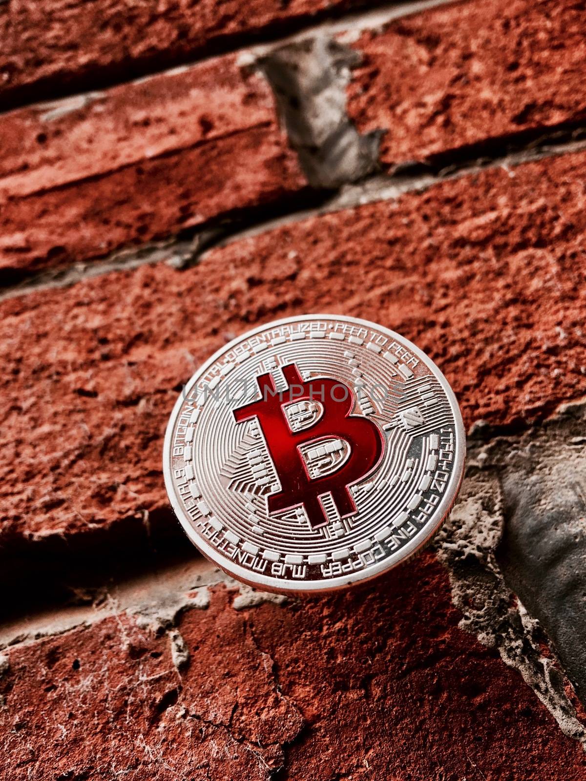 Digital currency physical silver bitcoin coin with red sign on brick wall.