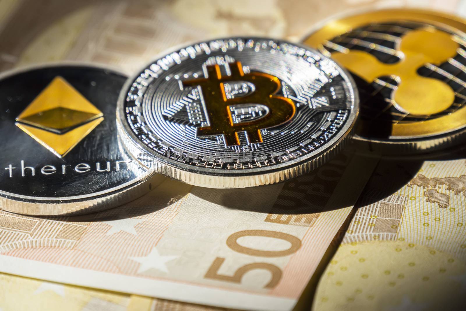 Cryptocurrency coins over euro banknotes; Bitcoin, Ethereum and Ripple coin