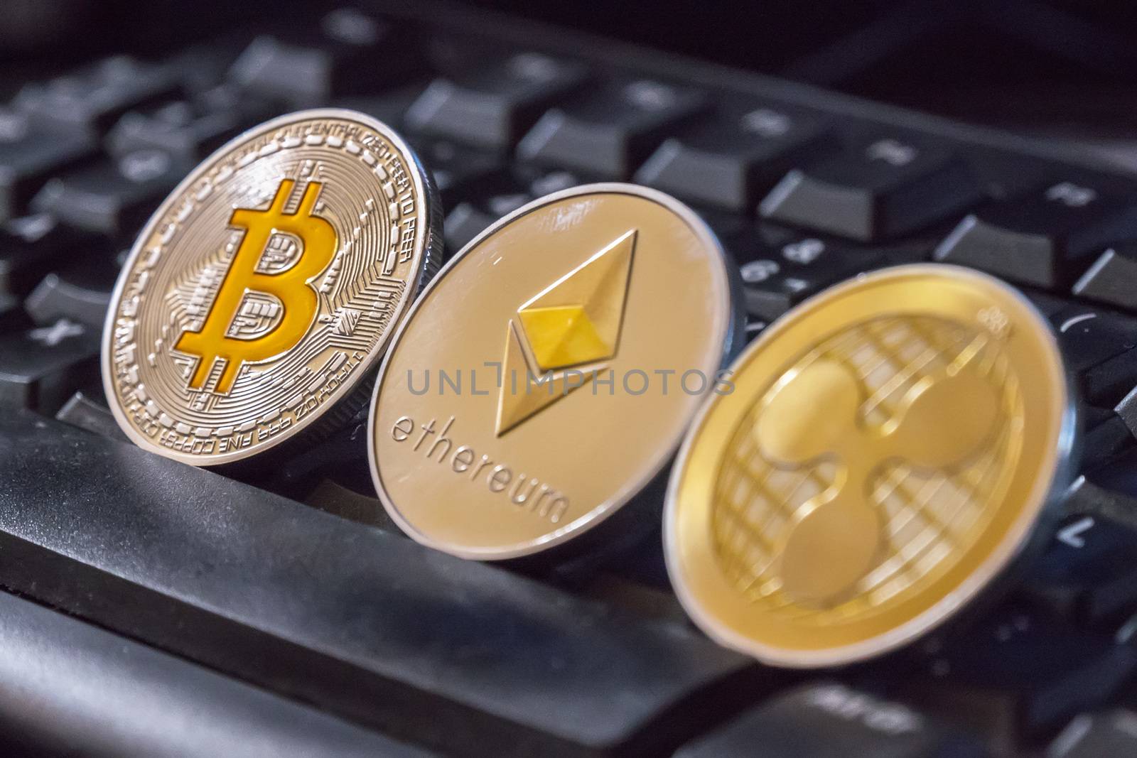 Cryptocurrency coins over black keyboard; Bitcoin, Ethereum and Ripple coins