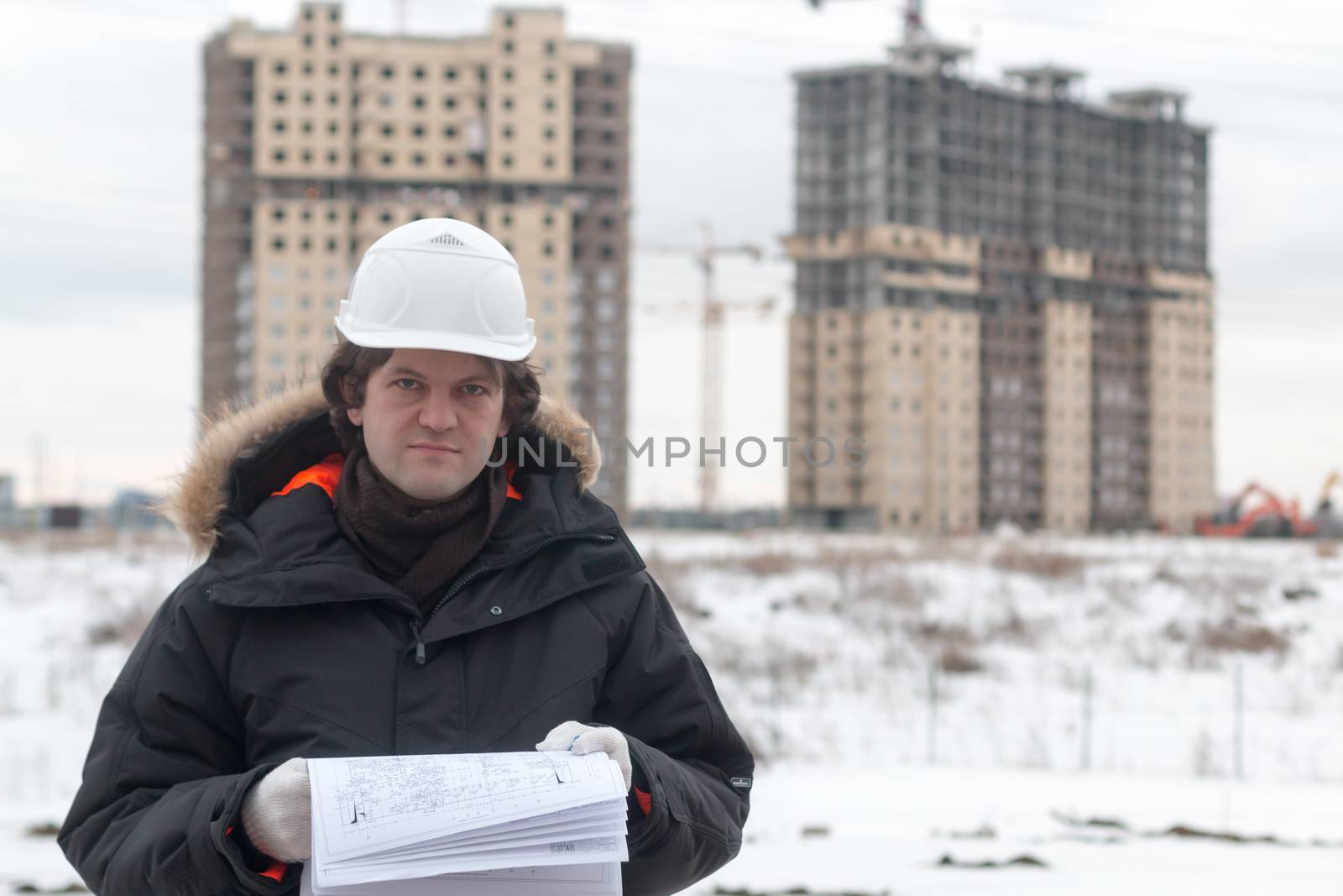 Worker or engineer holding drawing in hands and reading it on background of new apartment buildings and construction cranes on background. Architect engineer concept. Soft focus